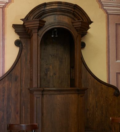 Zdjęcie nr 1: Konfesjonał o fantazyjnie wyciętej podstawie. Siedzisko ustawione na niskim cokole z drzwiczkami lekko wybrzuszonymi, ujętymi po bokach pilastrami, zdobionymi prostokątną płyciną i zamkniętymi profilowanym gzymsem. Powyżej pilastry zdobione kanelowaniem, zwieńczone wydatnymi, profilowanymi i ustawionymi pod kątem impostami. Przyczółek półkolisty, silnie profilowany. Ścianki zaplecka szerokie, zdobione wydłużonymi wolutami. W ściankach flankujących z boków siedzisko księdza prześwity z kratą.
