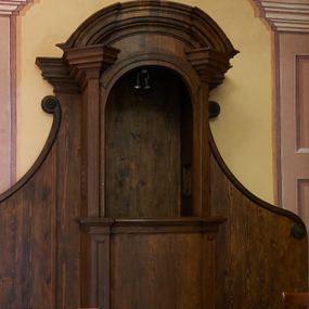 Zdjęcie nr 1: Konfesjonał o fantazyjnie wyciętej podstawie. Siedzisko ustawione na niskim cokole z drzwiczkami lekko wybrzuszonymi, ujętymi po bokach pilastrami, zdobionymi prostokątną płyciną i zamkniętymi profilowanym gzymsem. Powyżej pilastry zdobione kanelowaniem, zwieńczone wydatnymi, profilowanymi i ustawionymi pod kątem impostami. Przyczółek półkolisty, silnie profilowany. Ścianki zaplecka szerokie, zdobione wydłużonymi wolutami. W ściankach flankujących z boków siedzisko księdza prześwity z kratą.
