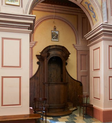 Zdjęcie nr 2: Konfesjonał o fantazyjnie wyciętej podstawie. Siedzisko ustawione na niskim cokole z drzwiczkami lekko wybrzuszonymi, ujętymi po bokach pilastrami, zdobionymi prostokątną płyciną i zamkniętymi profilowanym gzymsem. Powyżej pilastry zdobione kanelowaniem, zwieńczone wydatnymi, profilowanymi i ustawionymi pod kątem impostami. Przyczółek półkolisty, silnie profilowany. Ścianki zaplecka szerokie, zdobione wydłużonymi wolutami. W ściankach flankujących z boków siedzisko księdza prześwity z kratą.
