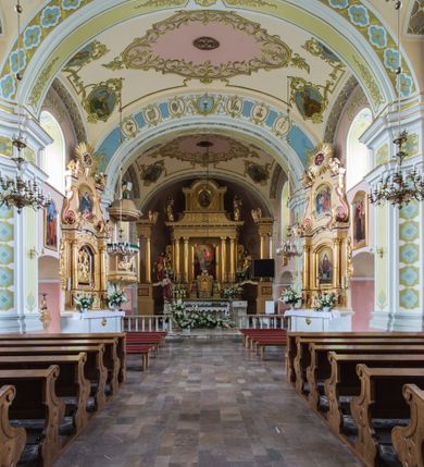 Zdjęcie nr 19: Orientowany kościół św. Wojciecha w Bulowicach obecnie uzyskał strukturę trójnawowej, trójprzęsłowej bazyliki z jednoprzęsłowym, nieco węższym prezbiterium zamkniętym spłaszczoną absydą. Na przedłużeniu dostawionych naw wybudowano półkolisty aneks zakrystyjny okalający apsydę, przepruwając go trzema półokrągłymi oknami oraz wejściem na osi. W aneksie od strony południowo-wschodniej urządzono otwartą na zewnątrz półkolistą arkadą kaplicę Ogrójcową. Od zachodu do nawy głównej przylega lekko wysunięta do przodu czworoboczna wieża flankowana dwoma, piętrowymi aneksami. Elewację masywu wieżowego artykułuje profilowany gzyms koronujący wyłamany na szerokości wieży, podtrzymujący miedziany daszek pulpitowy, dzielący ją na dwie kondygnacje. Podobny gzyms zamyka wieżę u góry, ponad którym wznosi się cebulasty hełm zwieńczony krzyżem na bani. Pod gzymsem w górnej części wieży usytuowano tarcze zegarowe oraz poniżej półokrągłe okna. W jej przyziemiu urządzono kruchtę, do której prowadzi portal uszaty z widocznym nad nim odcinkiem belkowania. Za pomocą symetrycznych spływów dostawione dwie nawy zostały połączone w spójną całość z masywem wieżowym. Do obu naw prowadzą półokrągłe arkady, w których urządzono otwarte przedsionki poprzedzające weście do kościoła. Nawę główną i prezbiterium nakryto dachem siodłowym. W jej części wschodniej nadwieszono wieżyczkę na sygnaturkę w kształcie sześciobocznej latarnii z baniastym hełmem i krzyżem. Nawy boczne i aneks zakrystyjny przykryto dachami pulpitowymi. Elewacje zewnętrzne zostały pozbawione artykulacji za wyjątkiem niskiego kamiennego cokołu obiegającego całą świątynię. Wnętrze nawy głównej zostało rozczłonkowane za pomocą opilastrowanych filarów, ponad którymi widoczne są odcinki belkowania. W tęczy kościoła zastosowano pilastry zdwojone. Nawy boczne połączono z nawą główną za pomocą mocno spłaszczonych arkad. Ponad nimi przepruto prostokątne okna zamknięte łukiem odcinkowym. Całość nawy nakryto sklepieniem żagielkowym wspartym na gurtach, zaś prezbiterium przykryto hemisferycznie. W części zachodniej nawy głównej zawieszono chór muzyczny wsparty na dwóch drewnianych filarach z drewnianym, pełnym parapetem artykułowanym czworobocznymi płycinami. Na osi środkowej parapet wyłamano na rzucie trapezu. W prezbiterium ustawiono ołtarz główny, a przy łuku tęczowym dwa ołtarze boczne. Na północnej ścianie łuku tęczowego zawieszono ambonę. Dwa niewielkie ołtarze boczne znalazły się także na zakończeniu naw bocznych.   