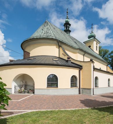 Zdjęcie nr 14: Orientowany kościół św. Wojciecha w Bulowicach obecnie uzyskał strukturę trójnawowej, trójprzęsłowej bazyliki z jednoprzęsłowym, nieco węższym prezbiterium zamkniętym spłaszczoną absydą. Na przedłużeniu dostawionych naw wybudowano półkolisty aneks zakrystyjny okalający apsydę, przepruwając go trzema półokrągłymi oknami oraz wejściem na osi. W aneksie od strony południowo-wschodniej urządzono otwartą na zewnątrz półkolistą arkadą kaplicę Ogrójcową. Od zachodu do nawy głównej przylega lekko wysunięta do przodu czworoboczna wieża flankowana dwoma, piętrowymi aneksami. Elewację masywu wieżowego artykułuje profilowany gzyms koronujący wyłamany na szerokości wieży, podtrzymujący miedziany daszek pulpitowy, dzielący ją na dwie kondygnacje. Podobny gzyms zamyka wieżę u góry, ponad którym wznosi się cebulasty hełm zwieńczony krzyżem na bani. Pod gzymsem w górnej części wieży usytuowano tarcze zegarowe oraz poniżej półokrągłe okna. W jej przyziemiu urządzono kruchtę, do której prowadzi portal uszaty z widocznym nad nim odcinkiem belkowania. Za pomocą symetrycznych spływów dostawione dwie nawy zostały połączone w spójną całość z masywem wieżowym. Do obu naw prowadzą półokrągłe arkady, w których urządzono otwarte przedsionki poprzedzające weście do kościoła. Nawę główną i prezbiterium nakryto dachem siodłowym. W jej części wschodniej nadwieszono wieżyczkę na sygnaturkę w kształcie sześciobocznej latarnii z baniastym hełmem i krzyżem. Nawy boczne i aneks zakrystyjny przykryto dachami pulpitowymi. Elewacje zewnętrzne zostały pozbawione artykulacji za wyjątkiem niskiego kamiennego cokołu obiegającego całą świątynię. Wnętrze nawy głównej zostało rozczłonkowane za pomocą opilastrowanych filarów, ponad którymi widoczne są odcinki belkowania. W tęczy kościoła zastosowano pilastry zdwojone. Nawy boczne połączono z nawą główną za pomocą mocno spłaszczonych arkad. Ponad nimi przepruto prostokątne okna zamknięte łukiem odcinkowym. Całość nawy nakryto sklepieniem żagielkowym wspartym na gurtach, zaś prezbiterium przykryto hemisferycznie. W części zachodniej nawy głównej zawieszono chór muzyczny wsparty na dwóch drewnianych filarach z drewnianym, pełnym parapetem artykułowanym czworobocznymi płycinami. Na osi środkowej parapet wyłamano na rzucie trapezu. W prezbiterium ustawiono ołtarz główny, a przy łuku tęczowym dwa ołtarze boczne. Na północnej ścianie łuku tęczowego zawieszono ambonę. Dwa niewielkie ołtarze boczne znalazły się także na zakończeniu naw bocznych.   