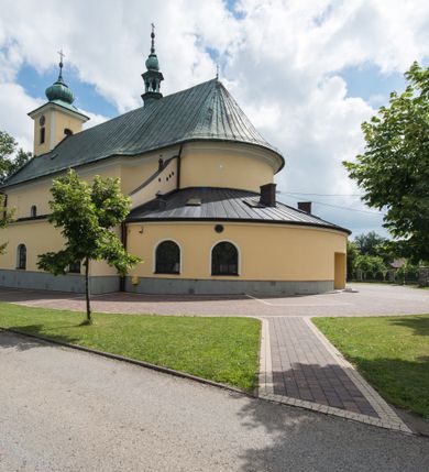 Zdjęcie nr 15: Orientowany kościół św. Wojciecha w Bulowicach obecnie uzyskał strukturę trójnawowej, trójprzęsłowej bazyliki z jednoprzęsłowym, nieco węższym prezbiterium zamkniętym spłaszczoną absydą. Na przedłużeniu dostawionych naw wybudowano półkolisty aneks zakrystyjny okalający apsydę, przepruwając go trzema półokrągłymi oknami oraz wejściem na osi. W aneksie od strony południowo-wschodniej urządzono otwartą na zewnątrz półkolistą arkadą kaplicę Ogrójcową. Od zachodu do nawy głównej przylega lekko wysunięta do przodu czworoboczna wieża flankowana dwoma, piętrowymi aneksami. Elewację masywu wieżowego artykułuje profilowany gzyms koronujący wyłamany na szerokości wieży, podtrzymujący miedziany daszek pulpitowy, dzielący ją na dwie kondygnacje. Podobny gzyms zamyka wieżę u góry, ponad którym wznosi się cebulasty hełm zwieńczony krzyżem na bani. Pod gzymsem w górnej części wieży usytuowano tarcze zegarowe oraz poniżej półokrągłe okna. W jej przyziemiu urządzono kruchtę, do której prowadzi portal uszaty z widocznym nad nim odcinkiem belkowania. Za pomocą symetrycznych spływów dostawione dwie nawy zostały połączone w spójną całość z masywem wieżowym. Do obu naw prowadzą półokrągłe arkady, w których urządzono otwarte przedsionki poprzedzające weście do kościoła. Nawę główną i prezbiterium nakryto dachem siodłowym. W jej części wschodniej nadwieszono wieżyczkę na sygnaturkę w kształcie sześciobocznej latarnii z baniastym hełmem i krzyżem. Nawy boczne i aneks zakrystyjny przykryto dachami pulpitowymi. Elewacje zewnętrzne zostały pozbawione artykulacji za wyjątkiem niskiego kamiennego cokołu obiegającego całą świątynię. Wnętrze nawy głównej zostało rozczłonkowane za pomocą opilastrowanych filarów, ponad którymi widoczne są odcinki belkowania. W tęczy kościoła zastosowano pilastry zdwojone. Nawy boczne połączono z nawą główną za pomocą mocno spłaszczonych arkad. Ponad nimi przepruto prostokątne okna zamknięte łukiem odcinkowym. Całość nawy nakryto sklepieniem żagielkowym wspartym na gurtach, zaś prezbiterium przykryto hemisferycznie. W części zachodniej nawy głównej zawieszono chór muzyczny wsparty na dwóch drewnianych filarach z drewnianym, pełnym parapetem artykułowanym czworobocznymi płycinami. Na osi środkowej parapet wyłamano na rzucie trapezu. W prezbiterium ustawiono ołtarz główny, a przy łuku tęczowym dwa ołtarze boczne. Na północnej ścianie łuku tęczowego zawieszono ambonę. Dwa niewielkie ołtarze boczne znalazły się także na zakończeniu naw bocznych.   