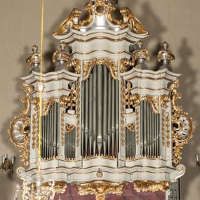 Zdjęcie nr 1: Szafa architektoniczna, pięcioosiowa, na falistym, profilowanym cokole, podtrzymywanym przez trzy ornamentalne wsporniki. Oś środkowa najwyższa, dwie skrajne niższe, ujęte pilastrami zakończonymi konsolami podtrzymującymi fragmenty falistego belkowania, z prześwitami na piszczałki w formie stojącego prostokąta. Osie środkowe najniższe, zakończone fragmentami niepełnego, falistego belkowania, z prześwitami na piszczałki w formie stojącego prostokąta. Oś środkowa zwieńczona ornamentalnym wolutowo-muszlowym szczytem z płaskorzeźbioną lirą oraz ornamentalnymi fragmentami przerwanego przyczółka. Na belkowaniu skrajnych osi ustawione cztery klasycystyczne wazony, a na belkowaniu osi środkowych cokoły z wicią roślinną. Trzony pilastrów dekorowane liściastymi zwisami. Prześwity na piszczałki w górnej części zdobione ornamentem roślinnym utworzonym z liści i kwiatów. Szafa flankowana rocaille'owymi uszami. Struktura polichromowana w kolorze białym, profile i ornamentyka złocone, detal srebrzony. 