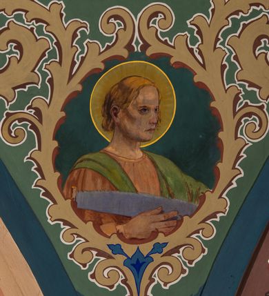 Zdjęcie nr 19: W prezbiterium w absydzie do dwóch trzecich wysokości ściany dekoracja roślinno-geometryczna z motywami kwiatowymi w kolorach zielono-turkusowym oraz złotym; powyżej dwa anioły na tle niebieskiego nieba z rozetami, całość zakończona zgeometryzowaną glorią promienistą uzupełnioną motywami kwiatowymi. 
Ściany boczne prezbiterium w kolorze jasnego różu; na ścianie tarczowej południowej medalion z kielichem i hostią w glorii promienistej. Na pilastrach, gurtach sklepiennych i w rozglifieniach okien symetryczna dekoracja roślinna. Na sklepieniu jasnopomarańczowe pole, w którego centrum znajduje się medalion z przedstawieniem Veraicon w glorii promienistej uzupełnionej motywami roślinnymi. 
Łuk tęczowy pokryty ornamentem roślinnym z motywami kłosów zbóż, na niebieskim tle, na środku łuku przedstawienie pelikana w gnieździe. Po wewnętrznej stronie łuku malatura w postaci fantazyjnego ornamentu roślinnego na beżowym tle. 
Ściany nawy gładkie, w kolorze zgaszonej, jasnej zieleni; z malowanymi zacheuszkami. W rozglifieniach okien symetryczna, stylizowana dekoracja arabeskowa na pomarańczowym i żółtym tle. Pilastry i łuki pokryte różnokolorowym, fantazyjnym ornamentem roślinnym. Sklepienia w każdym przęśle z wydzielonymi jasnożółtymi, owalnymi polami, w których centrum znajdują się niebieskie medaliony z przedstawieniem gorejącego serca lub monogramu IHS, w koronie cierniowej, w wieńcu z dekoracji roślinnej i w fioletowej glorii promienistej. W przyłuczach sklepień medaliony z przedstawieniami popiersi 12 apostołów, po czterech w każdym przęśle, ujętych żółtą wicią roślinną, na zielonym tle. Gurty sklepienne z motywem krzyży na żółto-pomarańczowym tle. 
Parapet chóru muzycznego i wspierające go arkady podzielone na malowane pola i płyciny wypełnione fantazyjnym ornamentem roślinnym. Na osi balustrady chóru przedstawienie liry. W podłuczu środkowej arkady pod chórem oko Opatrzności w wielobarwnej, stylizowanej glorii promienistej. 
Na ścianie zachodniej dwie półkoliście zamknięte nisze z przedstawieniami z lewej strony św. Cecylii grającej na organach, zaś z prawej króla Dawida grającego na harfie, na jasnoniebieskim tle. W rozglifieniach nisz stylizowana dekoracja geometryczno-roślinna. 
