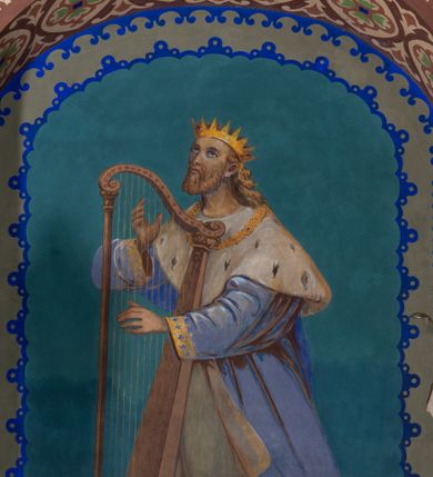 Zdjęcie nr 7: W prezbiterium w absydzie do dwóch trzecich wysokości ściany dekoracja roślinno-geometryczna z motywami kwiatowymi w kolorach zielono-turkusowym oraz złotym; powyżej dwa anioły na tle niebieskiego nieba z rozetami, całość zakończona zgeometryzowaną glorią promienistą uzupełnioną motywami kwiatowymi. 
Ściany boczne prezbiterium w kolorze jasnego różu; na ścianie tarczowej południowej medalion z kielichem i hostią w glorii promienistej. Na pilastrach, gurtach sklepiennych i w rozglifieniach okien symetryczna dekoracja roślinna. Na sklepieniu jasnopomarańczowe pole, w którego centrum znajduje się medalion z przedstawieniem Veraicon w glorii promienistej uzupełnionej motywami roślinnymi. 
Łuk tęczowy pokryty ornamentem roślinnym z motywami kłosów zbóż, na niebieskim tle, na środku łuku przedstawienie pelikana w gnieździe. Po wewnętrznej stronie łuku malatura w postaci fantazyjnego ornamentu roślinnego na beżowym tle. 
Ściany nawy gładkie, w kolorze zgaszonej, jasnej zieleni; z malowanymi zacheuszkami. W rozglifieniach okien symetryczna, stylizowana dekoracja arabeskowa na pomarańczowym i żółtym tle. Pilastry i łuki pokryte różnokolorowym, fantazyjnym ornamentem roślinnym. Sklepienia w każdym przęśle z wydzielonymi jasnożółtymi, owalnymi polami, w których centrum znajdują się niebieskie medaliony z przedstawieniem gorejącego serca lub monogramu IHS, w koronie cierniowej, w wieńcu z dekoracji roślinnej i w fioletowej glorii promienistej. W przyłuczach sklepień medaliony z przedstawieniami popiersi 12 apostołów, po czterech w każdym przęśle, ujętych żółtą wicią roślinną, na zielonym tle. Gurty sklepienne z motywem krzyży na żółto-pomarańczowym tle. 
Parapet chóru muzycznego i wspierające go arkady podzielone na malowane pola i płyciny wypełnione fantazyjnym ornamentem roślinnym. Na osi balustrady chóru przedstawienie liry. W podłuczu środkowej arkady pod chórem oko Opatrzności w wielobarwnej, stylizowanej glorii promienistej. 
Na ścianie zachodniej dwie półkoliście zamknięte nisze z przedstawieniami z lewej strony św. Cecylii grającej na organach, zaś z prawej króla Dawida grającego na harfie, na jasnoniebieskim tle. W rozglifieniach nisz stylizowana dekoracja geometryczno-roślinna. 
