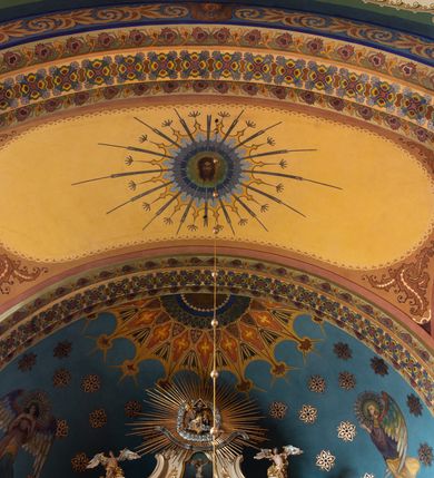 Zdjęcie nr 18: W prezbiterium w absydzie do dwóch trzecich wysokości ściany dekoracja roślinno-geometryczna z motywami kwiatowymi w kolorach zielono-turkusowym oraz złotym; powyżej dwa anioły na tle niebieskiego nieba z rozetami, całość zakończona zgeometryzowaną glorią promienistą uzupełnioną motywami kwiatowymi. 
Ściany boczne prezbiterium w kolorze jasnego różu; na ścianie tarczowej południowej medalion z kielichem i hostią w glorii promienistej. Na pilastrach, gurtach sklepiennych i w rozglifieniach okien symetryczna dekoracja roślinna. Na sklepieniu jasnopomarańczowe pole, w którego centrum znajduje się medalion z przedstawieniem Veraicon w glorii promienistej uzupełnionej motywami roślinnymi. 
Łuk tęczowy pokryty ornamentem roślinnym z motywami kłosów zbóż, na niebieskim tle, na środku łuku przedstawienie pelikana w gnieździe. Po wewnętrznej stronie łuku malatura w postaci fantazyjnego ornamentu roślinnego na beżowym tle. 
Ściany nawy gładkie, w kolorze zgaszonej, jasnej zieleni; z malowanymi zacheuszkami. W rozglifieniach okien symetryczna, stylizowana dekoracja arabeskowa na pomarańczowym i żółtym tle. Pilastry i łuki pokryte różnokolorowym, fantazyjnym ornamentem roślinnym. Sklepienia w każdym przęśle z wydzielonymi jasnożółtymi, owalnymi polami, w których centrum znajdują się niebieskie medaliony z przedstawieniem gorejącego serca lub monogramu IHS, w koronie cierniowej, w wieńcu z dekoracji roślinnej i w fioletowej glorii promienistej. W przyłuczach sklepień medaliony z przedstawieniami popiersi 12 apostołów, po czterech w każdym przęśle, ujętych żółtą wicią roślinną, na zielonym tle. Gurty sklepienne z motywem krzyży na żółto-pomarańczowym tle. 
Parapet chóru muzycznego i wspierające go arkady podzielone na malowane pola i płyciny wypełnione fantazyjnym ornamentem roślinnym. Na osi balustrady chóru przedstawienie liry. W podłuczu środkowej arkady pod chórem oko Opatrzności w wielobarwnej, stylizowanej glorii promienistej. 
Na ścianie zachodniej dwie półkoliście zamknięte nisze z przedstawieniami z lewej strony św. Cecylii grającej na organach, zaś z prawej króla Dawida grającego na harfie, na jasnoniebieskim tle. W rozglifieniach nisz stylizowana dekoracja geometryczno-roślinna. 
