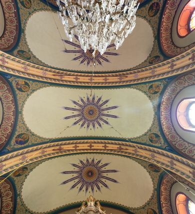 Zdjęcie nr 17: W prezbiterium w absydzie do dwóch trzecich wysokości ściany dekoracja roślinno-geometryczna z motywami kwiatowymi w kolorach zielono-turkusowym oraz złotym; powyżej dwa anioły na tle niebieskiego nieba z rozetami, całość zakończona zgeometryzowaną glorią promienistą uzupełnioną motywami kwiatowymi. 
Ściany boczne prezbiterium w kolorze jasnego różu; na ścianie tarczowej południowej medalion z kielichem i hostią w glorii promienistej. Na pilastrach, gurtach sklepiennych i w rozglifieniach okien symetryczna dekoracja roślinna. Na sklepieniu jasnopomarańczowe pole, w którego centrum znajduje się medalion z przedstawieniem Veraicon w glorii promienistej uzupełnionej motywami roślinnymi. 
Łuk tęczowy pokryty ornamentem roślinnym z motywami kłosów zbóż, na niebieskim tle, na środku łuku przedstawienie pelikana w gnieździe. Po wewnętrznej stronie łuku malatura w postaci fantazyjnego ornamentu roślinnego na beżowym tle. 
Ściany nawy gładkie, w kolorze zgaszonej, jasnej zieleni; z malowanymi zacheuszkami. W rozglifieniach okien symetryczna, stylizowana dekoracja arabeskowa na pomarańczowym i żółtym tle. Pilastry i łuki pokryte różnokolorowym, fantazyjnym ornamentem roślinnym. Sklepienia w każdym przęśle z wydzielonymi jasnożółtymi, owalnymi polami, w których centrum znajdują się niebieskie medaliony z przedstawieniem gorejącego serca lub monogramu IHS, w koronie cierniowej, w wieńcu z dekoracji roślinnej i w fioletowej glorii promienistej. W przyłuczach sklepień medaliony z przedstawieniami popiersi 12 apostołów, po czterech w każdym przęśle, ujętych żółtą wicią roślinną, na zielonym tle. Gurty sklepienne z motywem krzyży na żółto-pomarańczowym tle. 
Parapet chóru muzycznego i wspierające go arkady podzielone na malowane pola i płyciny wypełnione fantazyjnym ornamentem roślinnym. Na osi balustrady chóru przedstawienie liry. W podłuczu środkowej arkady pod chórem oko Opatrzności w wielobarwnej, stylizowanej glorii promienistej. 
Na ścianie zachodniej dwie półkoliście zamknięte nisze z przedstawieniami z lewej strony św. Cecylii grającej na organach, zaś z prawej króla Dawida grającego na harfie, na jasnoniebieskim tle. W rozglifieniach nisz stylizowana dekoracja geometryczno-roślinna. 
