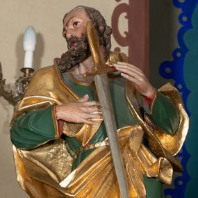 Zdjęcie nr 1: Rzeźba pełna, ustawiona na niskiej podstawie. Święty zwrócony frontalnie, z głową skierowaną w prawo, w kontrapoście, z silnie wypchniętym w bok lewym biodrem. Prawą rękę kładzie na piersi, lewą ugiętą unosi. Na tle piersi zamontowany miecz, skierowany ostrzem w dół. Twarz ma szczupłą, o dużych oczach, garbatym nosie i pełnych, rozchylonych ustach; okoloną gęstą brodą oraz krótkimi, kręconymi włosami. Ubrany jest w zieloną tunikę o złoconej lamówce, przepasaną w talii, odsłaniającą prawą nogę oraz złocony płaszcz narzucony na ramiona i zawieszony przy pasie z przodu postaci. Na stopach ma złocone buty z wysokimi, wywiniętymi cholewkami. Polichromia ciała naturalistyczna. 
