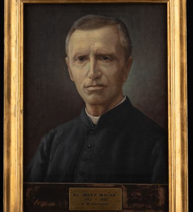 Zdjęcie nr 2: Portret uzyskał kształt stojącego prostokąta ujętego w złoconą, profilowaną ramę. Na ciemnym tle nieznacznie rozjaśnionym wokoło głowy przedstawiono w popiersiu duchownego nieznacznie ujętego w trzech czwartych w prawo. Jest to dojrzały mężczyzna z pociągłą twarzą, wysokim czołem, z krótkimi, siwiejącymi włosami zaczesanymi w grzywkę z przedziałkiem. Jego twarz charakteryzują jasna karnacja, wydatny nos, wąskie usta i niebieskie oczy. Widoczne są także uszy. Ubrany jest w czarną sutannę z białą koloratką pod szyją. Pod portretem umieszczono tabliczkę z napisem "Ks(iądz) JÓZEF MACAK / 1892-1896 / w Brzeszczach". 
