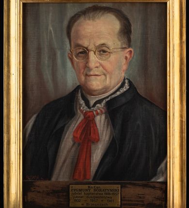 Zdjęcie nr 2: Portret uzyskał kształt stojącego prostokąta ujętego w złoconą, profilowaną ramę. Na rozjaśnionym tle przedstawiono w popiersiu duchownego nieznacznie ujętego w trzech czwartych w prawo. Jest to starszy mężczyzna w okrągłych okularach w złocistych oprawkach z pociągłą twarzą, wysokim czołem z zakolami ciemnych włosów zaczesanych do tyłu. Jego twarz charakteryzują jasna karnacja, widoczne zmarszczki, wydatny nos, wąskie usta i ciemne oczy. Widoczne są także uszy. Ubrany jest w czarny mantolet odsłaniający rokietę zawiązaną pod szyją czerwoną wstążką, spod której widać fragment sutanny z białą koloratką pod szyją. Pod portretem umocowano tabliczkę z napisem &quot;Ks(iądz) Can(onik) / ZYGMUNT BORATYŃSKI / jubilat kapłaństwa 1906-1957 / jubilat duszpasterstwa / 1932-1957 + 1961 / w Brzeszczach&quot;. 