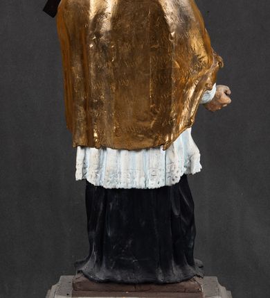 Zdjęcie nr 4: Feretron składa się z całopostaciowej rzeźby św. Jana Nepomucena ustawionej na niskim czworobocznym postumencie przymocowanym do rozbudowanego, profilowanego cokołu przeprutego w osiach skrajnych otworami na drążki do noszenia. Jan Nepomucen został ukazany frontalnie w nieznacznym kontrapoście. Na lewym przedramieniu trzyma krucyfiks z pasyjką od dołu wsparty prawą ręką. Święty ma owalną twarz z jasną karnacją o pełnych, rumianych policzkach, wydatnym nosie i ustach i szeroko otwartych oczach o spojrzeniu skierowanym na widza. Jego głowę otaczają krótkie, brązowe włosy widoczne spod biretu, który ma na głowie oraz krótka broda. Kapłan ubrany jest w czarną sutannę z parterami, białą komżę  dekorowaną u spodu koronką oraz pozłoconą almucję. 