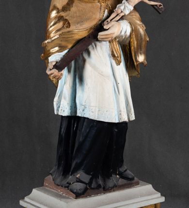 Zdjęcie nr 2: Feretron składa się z całopostaciowej rzeźby św. Jana Nepomucena ustawionej na niskim czworobocznym postumencie przymocowanym do rozbudowanego, profilowanego cokołu przeprutego w osiach skrajnych otworami na drążki do noszenia. Jan Nepomucen został ukazany frontalnie w nieznacznym kontrapoście. Na lewym przedramieniu trzyma krucyfiks z pasyjką od dołu wsparty prawą ręką. Święty ma owalną twarz z jasną karnacją o pełnych, rumianych policzkach, wydatnym nosie i ustach i szeroko otwartych oczach o spojrzeniu skierowanym na widza. Jego głowę otaczają krótkie, brązowe włosy widoczne spod biretu, który ma na głowie oraz krótka broda. Kapłan ubrany jest w czarną sutannę z parterami, białą komżę  dekorowaną u spodu koronką oraz pozłoconą almucję. 