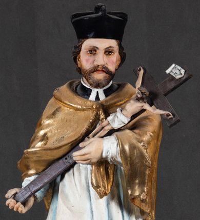 Zdjęcie nr 1: Feretron składa się z całopostaciowej rzeźby św. Jana Nepomucena ustawionej na niskim czworobocznym postumencie przymocowanym do rozbudowanego, profilowanego cokołu przeprutego w osiach skrajnych otworami na drążki do noszenia. Jan Nepomucen został ukazany frontalnie w nieznacznym kontrapoście. Na lewym przedramieniu trzyma krucyfiks z pasyjką od dołu wsparty prawą ręką. Święty ma owalną twarz z jasną karnacją o pełnych, rumianych policzkach, wydatnym nosie i ustach i szeroko otwartych oczach o spojrzeniu skierowanym na widza. Jego głowę otaczają krótkie, brązowe włosy widoczne spod biretu, który ma na głowie oraz krótka broda. Kapłan ubrany jest w czarną sutannę z parterami, białą komżę  dekorowaną u spodu koronką oraz pozłoconą almucję. 