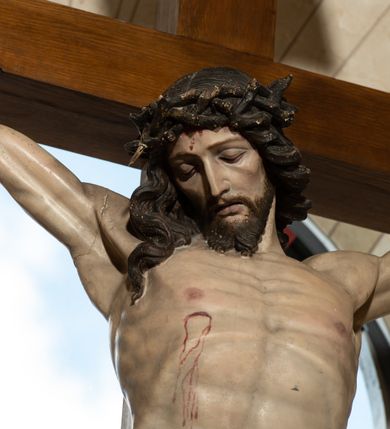 Zdjęcie nr 3: Na krzyżu z jasnego drewna zawieszono polichromowaną figurę martwego Chrystusa o szeroko rozpostartych ramionach. Ciało Zbawiciela do krzyża jest przymocowane za pomocą trzech gwoździ. On sam został ukazany jako martwy z zamkniętymi oczami i nieznacznie słaniającą się głową. Jego postać jest nieznacznie wysmuklona z naturalnie potraktowaną muskulaturą korpusu, zaznaczononą raną prawego boku. Nogi są lekko zwrółcone do osi środkowej, z założeniem prawej stopy na lewą. Twarz Zbawiciela jest mocno wychudła i pociągła. Charakteryzują ją zamknięte oczy, wydatny nos i usta. Otaczają ją brązowe włosy opadające puklami na kark oraz na prawe ramię oraz  brązowy zarost. Chrystus ma na głowie cierniową koronę, spod której na czoło spływają nieznaczne krople krwi. Biodra Zbawiciela przepasane są szarobiałym perizonium w formie zawoju z rozwianym festonem przy prawym boku. Tkaninę drapują ostre załamania. Ponad głową Chrystusa na pionowej belce krzyża zawieszono rozwiany titulus z napisem INRI przytwierdzone do krzyża wbitym na środku gwoździem. Całą figurę pokrywa naturalistyczna polichromia.