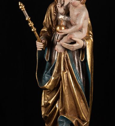 Zdjęcie nr 6: Rzeźba pełnoplastyczna, przyścienna. Przedstawienie Matki Boskiej z Dzieciątkiem ukazanej frontalnie, w całej postaci, w postawie stojącej, z ugiętymi w łokciach rękami; w prawej dłoni trzyma przed sobą berło, prawą obejmuje Dzieciątko. Twarz owalna, o jasnej karnacji, drobnych rysach, z wysokim czołem, okolona włosami spływającymi na ramiona i plecy. Na głowie złota otwarta korona (wtórna). Ubrana w długą suknię z długimi rękawami, zmarszczoną pionowymi równoległymi fałdami, przewiązaną w pasie. Na ramiona nałożony złoty płaszcz z błękitną podszewką, okrywający całą postać i odwijający się pod prawą ręką i przy podstawie okazałymi fałdami muszlowymi. Nagie Dzieciątko o pulchnym ciele siedzi na lewym przedramieniu Matki. Kulista głowa na krótkiej szyi okolona kędzierzawymi włosami. Prawą dłonią błogosławi, w lewej trzyma kulę. 