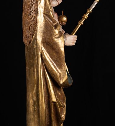 Zdjęcie nr 8: Rzeźba pełnoplastyczna, przyścienna. Przedstawienie Matki Boskiej z Dzieciątkiem ukazanej frontalnie, w całej postaci, w postawie stojącej, z ugiętymi w łokciach rękami; w prawej dłoni trzyma przed sobą berło, prawą obejmuje Dzieciątko. Twarz owalna, o jasnej karnacji, drobnych rysach, z wysokim czołem, okolona włosami spływającymi na ramiona i plecy. Na głowie złota otwarta korona (wtórna). Ubrana w długą suknię z długimi rękawami, zmarszczoną pionowymi równoległymi fałdami, przewiązaną w pasie. Na ramiona nałożony złoty płaszcz z błękitną podszewką, okrywający całą postać i odwijający się pod prawą ręką i przy podstawie okazałymi fałdami muszlowymi. Nagie Dzieciątko o pulchnym ciele siedzi na lewym przedramieniu Matki. Kulista głowa na krótkiej szyi okolona kędzierzawymi włosami. Prawą dłonią błogosławi, w lewej trzyma kulę. 