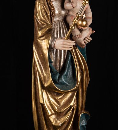 Zdjęcie nr 5: Rzeźba pełnoplastyczna, przyścienna. Przedstawienie Matki Boskiej z Dzieciątkiem ukazanej frontalnie, w całej postaci, w postawie stojącej, z ugiętymi w łokciach rękami; w prawej dłoni trzyma przed sobą berło, prawą obejmuje Dzieciątko. Twarz owalna, o jasnej karnacji, drobnych rysach, z wysokim czołem, okolona włosami spływającymi na ramiona i plecy. Na głowie złota otwarta korona (wtórna). Ubrana w długą suknię z długimi rękawami, zmarszczoną pionowymi równoległymi fałdami, przewiązaną w pasie. Na ramiona nałożony złoty płaszcz z błękitną podszewką, okrywający całą postać i odwijający się pod prawą ręką i przy podstawie okazałymi fałdami muszlowymi. Nagie Dzieciątko o pulchnym ciele siedzi na lewym przedramieniu Matki. Kulista głowa na krótkiej szyi okolona kędzierzawymi włosami. Prawą dłonią błogosławi, w lewej trzyma kulę. 