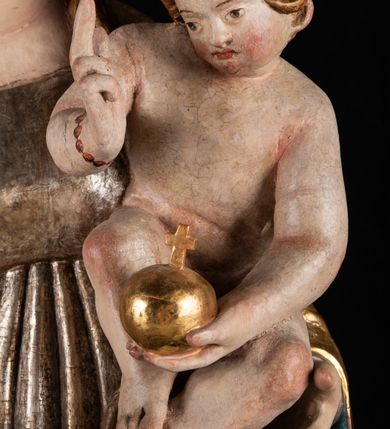 Zdjęcie nr 13: Rzeźba pełnoplastyczna, przyścienna. Przedstawienie Matki Boskiej z Dzieciątkiem ukazanej frontalnie, w całej postaci, w postawie stojącej, z ugiętymi w łokciach rękami; w prawej dłoni trzyma przed sobą berło, prawą obejmuje Dzieciątko. Twarz owalna, o jasnej karnacji, drobnych rysach, z wysokim czołem, okolona włosami spływającymi na ramiona i plecy. Na głowie złota otwarta korona (wtórna). Ubrana w długą suknię z długimi rękawami, zmarszczoną pionowymi równoległymi fałdami, przewiązaną w pasie. Na ramiona nałożony złoty płaszcz z błękitną podszewką, okrywający całą postać i odwijający się pod prawą ręką i przy podstawie okazałymi fałdami muszlowymi. Nagie Dzieciątko o pulchnym ciele siedzi na lewym przedramieniu Matki. Kulista głowa na krótkiej szyi okolona kędzierzawymi włosami. Prawą dłonią błogosławi, w lewej trzyma kulę. 