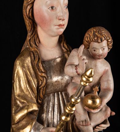 Zdjęcie nr 11: Rzeźba pełnoplastyczna, przyścienna. Przedstawienie Matki Boskiej z Dzieciątkiem ukazanej frontalnie, w całej postaci, w postawie stojącej, z ugiętymi w łokciach rękami; w prawej dłoni trzyma przed sobą berło, prawą obejmuje Dzieciątko. Twarz owalna, o jasnej karnacji, drobnych rysach, z wysokim czołem, okolona włosami spływającymi na ramiona i plecy. Na głowie złota otwarta korona (wtórna). Ubrana w długą suknię z długimi rękawami, zmarszczoną pionowymi równoległymi fałdami, przewiązaną w pasie. Na ramiona nałożony złoty płaszcz z błękitną podszewką, okrywający całą postać i odwijający się pod prawą ręką i przy podstawie okazałymi fałdami muszlowymi. Nagie Dzieciątko o pulchnym ciele siedzi na lewym przedramieniu Matki. Kulista głowa na krótkiej szyi okolona kędzierzawymi włosami. Prawą dłonią błogosławi, w lewej trzyma kulę. 