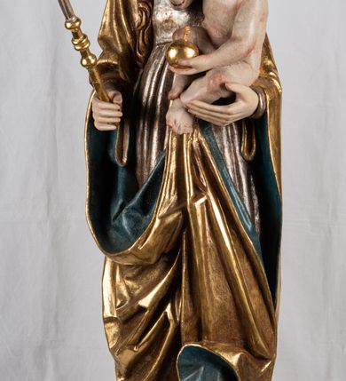 Zdjęcie nr 3: Rzeźba pełnoplastyczna, przyścienna. Przedstawienie Matki Boskiej z Dzieciątkiem ukazanej frontalnie, w całej postaci, w postawie stojącej, z ugiętymi w łokciach rękami; w prawej dłoni trzyma przed sobą berło, prawą obejmuje Dzieciątko. Twarz owalna, o jasnej karnacji, drobnych rysach, z wysokim czołem, okolona włosami spływającymi na ramiona i plecy. Na głowie złota otwarta korona (wtórna). Ubrana w długą suknię z długimi rękawami, zmarszczoną pionowymi równoległymi fałdami, przewiązaną w pasie. Na ramiona nałożony złoty płaszcz z błękitną podszewką, okrywający całą postać i odwijający się pod prawą ręką i przy podstawie okazałymi fałdami muszlowymi. Nagie Dzieciątko o pulchnym ciele siedzi na lewym przedramieniu Matki. Kulista głowa na krótkiej szyi okolona kędzierzawymi włosami. Prawą dłonią błogosławi, w lewej trzyma kulę. 