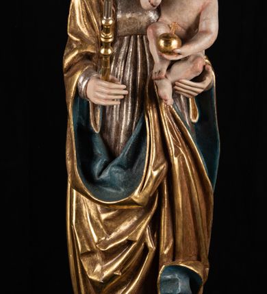 Zdjęcie nr 4: Rzeźba pełnoplastyczna, przyścienna. Przedstawienie Matki Boskiej z Dzieciątkiem ukazanej frontalnie, w całej postaci, w postawie stojącej, z ugiętymi w łokciach rękami; w prawej dłoni trzyma przed sobą berło, prawą obejmuje Dzieciątko. Twarz owalna, o jasnej karnacji, drobnych rysach, z wysokim czołem, okolona włosami spływającymi na ramiona i plecy. Na głowie złota otwarta korona (wtórna). Ubrana w długą suknię z długimi rękawami, zmarszczoną pionowymi równoległymi fałdami, przewiązaną w pasie. Na ramiona nałożony złoty płaszcz z błękitną podszewką, okrywający całą postać i odwijający się pod prawą ręką i przy podstawie okazałymi fałdami muszlowymi. Nagie Dzieciątko o pulchnym ciele siedzi na lewym przedramieniu Matki. Kulista głowa na krótkiej szyi okolona kędzierzawymi włosami. Prawą dłonią błogosławi, w lewej trzyma kulę. 