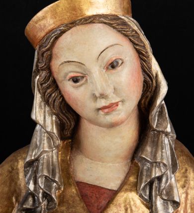 Zdjęcie nr 9: Rzeźba pełnoplastyczna, przyścienna, z tyłu wydrążona. Całopostaciowe przedstawienie tronującej Matki Boskiej z Dzieciątkiem. Maria, ukazana frontalnie, jako młoda kobieta, siedzi z rozstawionymi kolanami, z łukowato przegiętym w lewo tułowiem i głową lekko przechyloną w prawo. Ugiętymi w łokciach rękami podtrzymuje przed sobą Dzieciątko. Twarz Marii owalna, pełna, o jasnej karnacji, z szeroko rozstawionymi oczami, regularnymi łukami brwiowymi i refleksem uśmiechu na ustach. Głowę okrywa srebrzona chusta, opadająca na ramiona dwiema kaskadami rurkowatych fałdów, spod której widać krótkie brązowe włosy. Na głowie niski złoty diadem. Maria ubrana w długą srebrną, przewiązaną w pasie suknię, spod fałdów której widać czubki srebrnych butów. Na ramiona ma narzucony złocony płaszcz spięty na piersiach i okrywający kaskadami dekoracyjnych fałdów biodra i nogi Marii oraz ławę, na której siedzi. Nagie Dzieciątko o dużej głowie i wątłym ciele siedzi bokiem na kolanach Marii, twarz zwracając ku widzowi. Lewą ręką dotyka piersi Matki, w prawej trzyma błękitną kulę. 