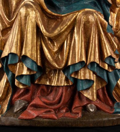 Zdjęcie nr 13: Rzeźba pełnoplastyczna, przyścienna, z tyłu wydrążona. Całopostaciowe przedstawienie tronującej Matki Boskiej z Dzieciątkiem. Maria, ukazana frontalnie, jako młoda kobieta, siedzi z rozstawionymi kolanami, z łukowato przegiętym w lewo tułowiem i głową lekko przechyloną w prawo. Ugiętymi w łokciach rękami podtrzymuje przed sobą Dzieciątko. Twarz Marii owalna, pełna, o jasnej karnacji, z szeroko rozstawionymi oczami, regularnymi łukami brwiowymi i refleksem uśmiechu na ustach. Głowę okrywa srebrzona chusta, opadająca na ramiona dwiema kaskadami rurkowatych fałdów, spod której widać krótkie brązowe włosy. Na głowie niski złoty diadem. Maria ubrana w długą srebrną, przewiązaną w pasie suknię, spod fałdów której widać czubki srebrnych butów. Na ramiona ma narzucony złocony płaszcz spięty na piersiach i okrywający kaskadami dekoracyjnych fałdów biodra i nogi Marii oraz ławę, na której siedzi. Nagie Dzieciątko o dużej głowie i wątłym ciele siedzi bokiem na kolanach Marii, twarz zwracając ku widzowi. Lewą ręką dotyka piersi Matki, w prawej trzyma błękitną kulę. 