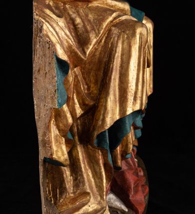 Zdjęcie nr 15: Rzeźba pełnoplastyczna, przyścienna, z tyłu wydrążona. Całopostaciowe przedstawienie tronującej Matki Boskiej z Dzieciątkiem. Maria, ukazana frontalnie, jako młoda kobieta, siedzi z rozstawionymi kolanami, z łukowato przegiętym w lewo tułowiem i głową lekko przechyloną w prawo. Ugiętymi w łokciach rękami podtrzymuje przed sobą Dzieciątko. Twarz Marii owalna, pełna, o jasnej karnacji, z szeroko rozstawionymi oczami, regularnymi łukami brwiowymi i refleksem uśmiechu na ustach. Głowę okrywa srebrzona chusta, opadająca na ramiona dwiema kaskadami rurkowatych fałdów, spod której widać krótkie brązowe włosy. Na głowie niski złoty diadem. Maria ubrana w długą srebrną, przewiązaną w pasie suknię, spod fałdów której widać czubki srebrnych butów. Na ramiona ma narzucony złocony płaszcz spięty na piersiach i okrywający kaskadami dekoracyjnych fałdów biodra i nogi Marii oraz ławę, na której siedzi. Nagie Dzieciątko o dużej głowie i wątłym ciele siedzi bokiem na kolanach Marii, twarz zwracając ku widzowi. Lewą ręką dotyka piersi Matki, w prawej trzyma błękitną kulę. 