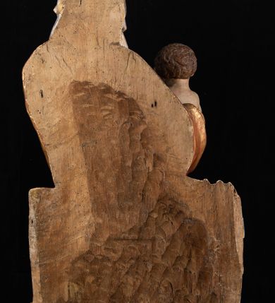 Zdjęcie nr 20: Rzeźba pełnoplastyczna, przyścienna, z tyłu wydrążona. Całopostaciowe przedstawienie tronującej Matki Boskiej z Dzieciątkiem. Maria, ukazana frontalnie, jako młoda kobieta, siedzi z rozstawionymi kolanami, z łukowato przegiętym w lewo tułowiem i głową lekko przechyloną w prawo. Ugiętymi w łokciach rękami podtrzymuje przed sobą Dzieciątko. Twarz Marii owalna, pełna, o jasnej karnacji, z szeroko rozstawionymi oczami, regularnymi łukami brwiowymi i refleksem uśmiechu na ustach. Głowę okrywa srebrzona chusta, opadająca na ramiona dwiema kaskadami rurkowatych fałdów, spod której widać krótkie brązowe włosy. Na głowie niski złoty diadem. Maria ubrana w długą srebrną, przewiązaną w pasie suknię, spod fałdów której widać czubki srebrnych butów. Na ramiona ma narzucony złocony płaszcz spięty na piersiach i okrywający kaskadami dekoracyjnych fałdów biodra i nogi Marii oraz ławę, na której siedzi. Nagie Dzieciątko o dużej głowie i wątłym ciele siedzi bokiem na kolanach Marii, twarz zwracając ku widzowi. Lewą ręką dotyka piersi Matki, w prawej trzyma błękitną kulę. 