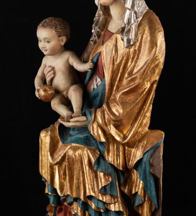 Zdjęcie nr 3: Rzeźba pełnoplastyczna, przyścienna, z tyłu wydrążona. Całopostaciowe przedstawienie tronującej Matki Boskiej z Dzieciątkiem. Maria, ukazana frontalnie, jako młoda kobieta, siedzi z rozstawionymi kolanami, z łukowato przegiętym w lewo tułowiem i głową lekko przechyloną w prawo. Ugiętymi w łokciach rękami podtrzymuje przed sobą Dzieciątko. Twarz Marii owalna, pełna, o jasnej karnacji, z szeroko rozstawionymi oczami, regularnymi łukami brwiowymi i refleksem uśmiechu na ustach. Głowę okrywa srebrzona chusta, opadająca na ramiona dwiema kaskadami rurkowatych fałdów, spod której widać krótkie brązowe włosy. Na głowie niski złoty diadem. Maria ubrana w długą srebrną, przewiązaną w pasie suknię, spod fałdów której widać czubki srebrnych butów. Na ramiona ma narzucony złocony płaszcz spięty na piersiach i okrywający kaskadami dekoracyjnych fałdów biodra i nogi Marii oraz ławę, na której siedzi. Nagie Dzieciątko o dużej głowie i wątłym ciele siedzi bokiem na kolanach Marii, twarz zwracając ku widzowi. Lewą ręką dotyka piersi Matki, w prawej trzyma błękitną kulę. 