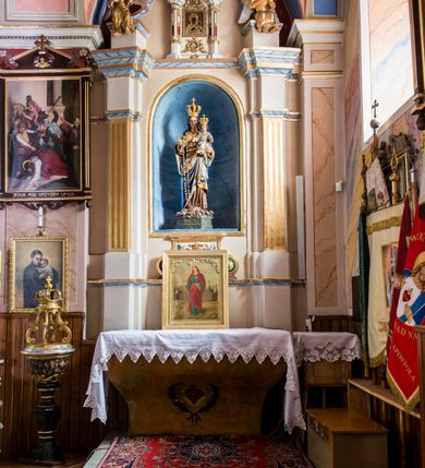 Zdjęcie nr 2: Ołtarz przyścienny, architektoniczny, jednoosiowy, jednokondygnacyjny ze zwieńczeniem. Ołtarz sarkofagowy z murowaną mensą i polichromowanym antepedium z motywem gorejącego serca Marii ujętego parą gałązek laurowych. Część środkową flankuje para zdwojonych lizen osadzonych na wysokich cokołach. Ustawione lekko skośnie na zewnątrz podpory wspierają przerwane i wyłamujące się ponad nimi belkowanie. Pole części środkowej i partii belkowania zajmuje nisza w kształcie stojącego prostokąta zamkniętego półkoliście. Zwieńczenie retabulum ujęte jest parą spływów oraz prostopadłościennych cokołów. Szczyt jest w formie trójkątnego przyczółka. W niszy części środkowej znajduje się figura Madonny z Dzieciątkiem. W zwieńczeniu natomiast jest niewielki obraz Matki Boskiej Częstochowskiej w obramieniu w formie architektonicznej nastawy ołtarzowej ujętej parą osadzonych na wysokich cokołach, ustawionych skośnie na zewnątrz filarów wspierających wyłamujące się ponad nimi przerwane belkowanie. Zwieńczenie ujmuje para ornamentalnych spływów wolutowych. Poniżej obrazu znajduje się relikwiarz ujęty ornamentyką rokokową, natomiast powyżej jest monogram maryjny w bogatej dekoracji ornamentalnej. Pośrodku zwieńczenia jest promienista gloria. Struktura biała, detale w kolorze czerwonym i złocone. W polu przyczółka w szczycie ołtarza jest oko Opatrzności Bożej. Na ujmujących zwieńczenie cokołach znajduje się para figur siedzących aniołów w złoconych szatach. Kolorystyka struktury retabulum utrzymana w kolorze beżowym, detal architektoniczny marmoryzowany w odcieniach błękitu i złocony.