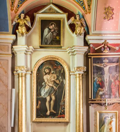 Zdjęcie nr 1: Ołtarz przyścienny, architektoniczny, jednoosiowy, jednokondygnacyjny ze zwieńczeniem. Ołtarz sarkofagowy z murowaną mensą i polichromowanym antepedium z motywem krzyża z koroną cierniową pośrodku. Część środkowa ujęta jest parą półkolumn osadzonych na postumentach  i przylegających do pary pilastrów. Ustawione lekko skośnie na zewnątrz podpory wspierają przerwane i wyłamujący się ponad nimi wysoki fryz oraz gzyms. Pole części środkowej i partii belkowania zajmuje płytka wnęka w kształcie stojącego prostokąta zamkniętego półkoliście. Zwieńczenie retabulum ujęte jest parą spływów oraz prostopadłościennych cokołów. Szczyt jest w formie trójkątnego przyczółka. Obraz w części środkowej ma kształt stojącego prostokąta zamkniętego półkoliście i przedstawia Męża Boleści wśród narzędzi męki Pańskiej. W zwieńczeniu jest obraz w kształcie stojącego prostokąta z wizerunkiem św. Stanisława Kostki. Pole przyczółka wypełnia polichromia przedstawiająca oko Opatrzności Bożej. Na ujmujących zwieńczenie cokołach znajduje się para figur siedzących aniołów w złoconych szatach. Kolorystyka struktury retabulum utrzymana jest w kolorze białym i jasnożółtym, detal architektoniczny jest złocony.         