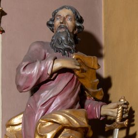 Zdjęcie nr 1: Rzeźba całopostaciowa przedstawia stojącego w wydatnym kontrapoście, na niewysokim postumencie św. Pawła zwróconego na wprost, z głową skierowaną w trzech czwartych w prawo. Twarz świętego charakteryzuje śniada karnacja, wyraziste rysy oraz długi, brązowy zarost. Półdługie, kręcone włosy opadają na kark mężczyzny. Święty ma na sobie długą, jasnoliliową suknię. Połę narzuconego na lewe ramię, rozwianego, złoconego płaszcza osłaniającego lewe biodro, podtrzymuje na wysokości klatki piersiowej prawą ręką. W lewej, zgiętej w łokciu i uniesionej na wysokości talii podtrzymuje miecz o złoconej rękojeści i srebrzonym ostrzu skierowanym w dół. 
