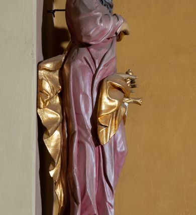 Zdjęcie nr 5: Rzeźba całopostaciowa przedstawia stojącego w wydatnym kontrapoście, na niewysokim postumencie św. Pawła zwróconego na wprost, z głową skierowaną w trzech czwartych w prawo. Twarz świętego charakteryzuje śniada karnacja, wyraziste rysy oraz długi, brązowy zarost. Półdługie, kręcone włosy opadają na kark mężczyzny. Święty ma na sobie długą, jasnoliliową suknię. Połę narzuconego na lewe ramię, rozwianego, złoconego płaszcza osłaniającego lewe biodro, podtrzymuje na wysokości klatki piersiowej prawą ręką. W lewej, zgiętej w łokciu i uniesionej na wysokości talii podtrzymuje miecz o złoconej rękojeści i srebrzonym ostrzu skierowanym w dół. 