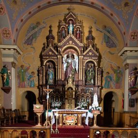 Zdjęcie nr 1: Ołtarz architektoniczny, jednokondygnacyjny, trójosiowy, ze zwieńczeniem. Ołtarz w formie prostopadłościanu z drewnianą mensą i antepedium artykułowanym półkolumienkami, pomiędzy którymi są płytkie wnęki zamknięte półkoliście z płaskorzeźbionymi wizerunkami 4 ewangelistów. Na mensie tabernakulum w formie prostopadłościennej szafki zwieńczone jest tronem wystawienia w kształcie baldachimu wspartego na podwójnych parach kolumienek, zwieńczonego po środku ażurową latarnią z kopułą oraz pinaklami na narożach. Po bokach tabernakulum ujmuje rząd trzech, osadzonych na wysokim cokole niszy z figurami aniołów.  
Retabulum osadzone jest na zdwojonym cokole. Predella artykułowana jest płaskorzeźbionymi płycinami w kształcie zbliżonym do kwadratu, wydzielonymi smukłymi cokołami, na których osadzone są kolumienki ujmujące osie części środkowej retabulum. Każda z osi ma formę prostokątnej niszy zamkniętej łukiem półkolistym. Niszę środkową ujmuje para kolumienek wspierających przerwane w partii architrawu i fryzu belkowanie oraz gzyms wieńczący, przybierający kształt trójkątnego przyczółka, wspierany dodatkowo parą kolumienek w partii fryzu. Nisze boczne ujmują pojedyncze pary kolumienek wspierających przerwany architraw i fryz oraz trójkątny przyczółek. Dodatkowo boki części środkowej retabulum ujmuje para niewielkich, ażurowych uszaków w formie przypór.  Zwieńczenie części środkowej tworzy struktura trójprzelotowego łuku triumfalnego zamkniętego po środku gzymsem w kształcie trójkątnego przyczółka. Zwieńczenia osi bocznych są w formie latarni zamkniętych kopułami. W osi środkowej znajduje się figura św. Michała Archanioła, po lewej św. Wojciecha, po prawej św. Stanisława. W zwieńczeniu, po środku jest rzeźba Matki Boskiej Niepokalanie Poczętej, po lewej św. Floriana, po prawej św. Kazimierza Jagiellończyka. Strukturę retabulum zdobi stylizowana, płaskorzeźbiona i malowana ornamentyka roślinna. Kolorystyka ołtarza utrzymana jest w odcieniach brązów, ornamentyka jest złocona. 

