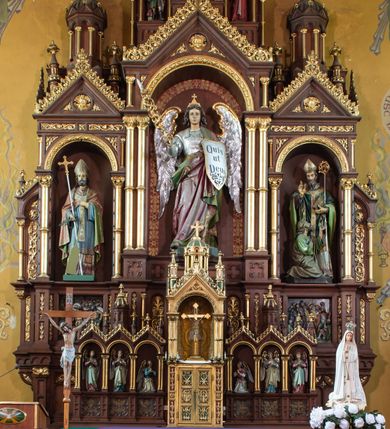 Zdjęcie nr 4: Ołtarz architektoniczny, jednokondygnacyjny, trójosiowy, ze zwieńczeniem. Ołtarz w formie prostopadłościanu z drewnianą mensą i antepedium artykułowanym półkolumienkami, pomiędzy którymi są płytkie wnęki zamknięte półkoliście z płaskorzeźbionymi wizerunkami 4 ewangelistów. Na mensie tabernakulum w formie prostopadłościennej szafki zwieńczone jest tronem wystawienia w kształcie baldachimu wspartego na podwójnych parach kolumienek, zwieńczonego po środku ażurową latarnią z kopułą oraz pinaklami na narożach. Po bokach tabernakulum ujmuje rząd trzech, osadzonych na wysokim cokole niszy z figurami aniołów.  
Retabulum osadzone jest na zdwojonym cokole. Predella artykułowana jest płaskorzeźbionymi płycinami w kształcie zbliżonym do kwadratu, wydzielonymi smukłymi cokołami, na których osadzone są kolumienki ujmujące osie części środkowej retabulum. Każda z osi ma formę prostokątnej niszy zamkniętej łukiem półkolistym. Niszę środkową ujmuje para kolumienek wspierających przerwane w partii architrawu i fryzu belkowanie oraz gzyms wieńczący, przybierający kształt trójkątnego przyczółka, wspierany dodatkowo parą kolumienek w partii fryzu. Nisze boczne ujmują pojedyncze pary kolumienek wspierających przerwany architraw i fryz oraz trójkątny przyczółek. Dodatkowo boki części środkowej retabulum ujmuje para niewielkich, ażurowych uszaków w formie przypór.  Zwieńczenie części środkowej tworzy struktura trójprzelotowego łuku triumfalnego zamkniętego po środku gzymsem w kształcie trójkątnego przyczółka. Zwieńczenia osi bocznych są w formie latarni zamkniętych kopułami. W osi środkowej znajduje się figura św. Michała Archanioła, po lewej św. Wojciecha, po prawej św. Stanisława. W zwieńczeniu, po środku jest rzeźba Matki Boskiej Niepokalanie Poczętej, po lewej św. Floriana, po prawej św. Kazimierza Jagiellończyka. Strukturę retabulum zdobi stylizowana, płaskorzeźbiona i malowana ornamentyka roślinna. Kolorystyka ołtarza utrzymana jest w odcieniach brązów, ornamentyka jest złocona. 

