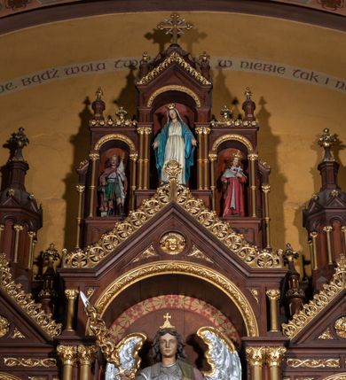 Zdjęcie nr 9: Ołtarz architektoniczny, jednokondygnacyjny, trójosiowy, ze zwieńczeniem. Ołtarz w formie prostopadłościanu z drewnianą mensą i antepedium artykułowanym półkolumienkami, pomiędzy którymi są płytkie wnęki zamknięte półkoliście z płaskorzeźbionymi wizerunkami 4 ewangelistów. Na mensie tabernakulum w formie prostopadłościennej szafki zwieńczone jest tronem wystawienia w kształcie baldachimu wspartego na podwójnych parach kolumienek, zwieńczonego po środku ażurową latarnią z kopułą oraz pinaklami na narożach. Po bokach tabernakulum ujmuje rząd trzech, osadzonych na wysokim cokole niszy z figurami aniołów.  
Retabulum osadzone jest na zdwojonym cokole. Predella artykułowana jest płaskorzeźbionymi płycinami w kształcie zbliżonym do kwadratu, wydzielonymi smukłymi cokołami, na których osadzone są kolumienki ujmujące osie części środkowej retabulum. Każda z osi ma formę prostokątnej niszy zamkniętej łukiem półkolistym. Niszę środkową ujmuje para kolumienek wspierających przerwane w partii architrawu i fryzu belkowanie oraz gzyms wieńczący, przybierający kształt trójkątnego przyczółka, wspierany dodatkowo parą kolumienek w partii fryzu. Nisze boczne ujmują pojedyncze pary kolumienek wspierających przerwany architraw i fryz oraz trójkątny przyczółek. Dodatkowo boki części środkowej retabulum ujmuje para niewielkich, ażurowych uszaków w formie przypór.  Zwieńczenie części środkowej tworzy struktura trójprzelotowego łuku triumfalnego zamkniętego po środku gzymsem w kształcie trójkątnego przyczółka. Zwieńczenia osi bocznych są w formie latarni zamkniętych kopułami. W osi środkowej znajduje się figura św. Michała Archanioła, po lewej św. Wojciecha, po prawej św. Stanisława. W zwieńczeniu, po środku jest rzeźba Matki Boskiej Niepokalanie Poczętej, po lewej św. Floriana, po prawej św. Kazimierza Jagiellończyka. Strukturę retabulum zdobi stylizowana, płaskorzeźbiona i malowana ornamentyka roślinna. Kolorystyka ołtarza utrzymana jest w odcieniach brązów, ornamentyka jest złocona. 

