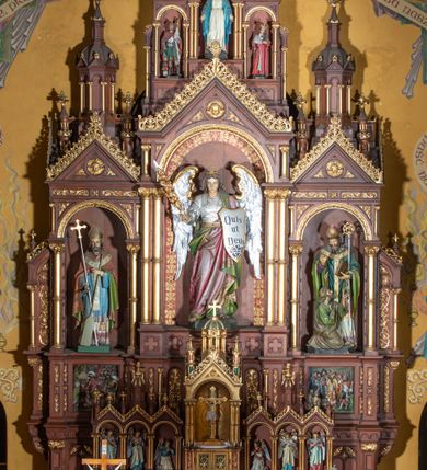 Zdjęcie nr 3: Ołtarz architektoniczny, jednokondygnacyjny, trójosiowy, ze zwieńczeniem. Ołtarz w formie prostopadłościanu z drewnianą mensą i antepedium artykułowanym półkolumienkami, pomiędzy którymi są płytkie wnęki zamknięte półkoliście z płaskorzeźbionymi wizerunkami 4 ewangelistów. Na mensie tabernakulum w formie prostopadłościennej szafki zwieńczone jest tronem wystawienia w kształcie baldachimu wspartego na podwójnych parach kolumienek, zwieńczonego po środku ażurową latarnią z kopułą oraz pinaklami na narożach. Po bokach tabernakulum ujmuje rząd trzech, osadzonych na wysokim cokole niszy z figurami aniołów.  
Retabulum osadzone jest na zdwojonym cokole. Predella artykułowana jest płaskorzeźbionymi płycinami w kształcie zbliżonym do kwadratu, wydzielonymi smukłymi cokołami, na których osadzone są kolumienki ujmujące osie części środkowej retabulum. Każda z osi ma formę prostokątnej niszy zamkniętej łukiem półkolistym. Niszę środkową ujmuje para kolumienek wspierających przerwane w partii architrawu i fryzu belkowanie oraz gzyms wieńczący, przybierający kształt trójkątnego przyczółka, wspierany dodatkowo parą kolumienek w partii fryzu. Nisze boczne ujmują pojedyncze pary kolumienek wspierających przerwany architraw i fryz oraz trójkątny przyczółek. Dodatkowo boki części środkowej retabulum ujmuje para niewielkich, ażurowych uszaków w formie przypór.  Zwieńczenie części środkowej tworzy struktura trójprzelotowego łuku triumfalnego zamkniętego po środku gzymsem w kształcie trójkątnego przyczółka. Zwieńczenia osi bocznych są w formie latarni zamkniętych kopułami. W osi środkowej znajduje się figura św. Michała Archanioła, po lewej św. Wojciecha, po prawej św. Stanisława. W zwieńczeniu, po środku jest rzeźba Matki Boskiej Niepokalanie Poczętej, po lewej św. Floriana, po prawej św. Kazimierza Jagiellończyka. Strukturę retabulum zdobi stylizowana, płaskorzeźbiona i malowana ornamentyka roślinna. Kolorystyka ołtarza utrzymana jest w odcieniach brązów, ornamentyka jest złocona. 

