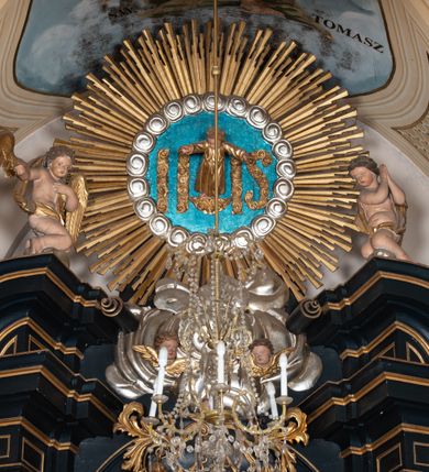Zdjęcie nr 2: Przyścienna, jednoosiowa i jednokondygnacyjna struktura ołtarza uzyskała kształt nastawy architektonicznej ze zwieńczeniem. Drewniany stipes ołtarzowy przyjął formę leżącego prostopadłościanu podtrzymującego mensę, ustawionego na dwustopniowym podeście. Drewniane antependium ujęto profilowaną ramą z polem udekorowanym monogramem maryjnym w centrum, otoczonym rzeźbionym różańcem przy zewnętrznych krawędziach. Stipes przylega do  trzystrefowego, wysokiego cokołu wspierającego nastawę. Kolejne strefy zostały wydzielone za pomocą poziomych profili. Drugą i trzecią strefę cokołu ozdobiono obramionymi, prostokątnymi płycinami - w drugiej strefie w kształcie stojących prostokątów, a w trzeciej leżących. Kondygnację wsparto na zdwojonych pilastrach o korynckich głowicach, przed którymi ustawiono korynckie kolumny podtrzymujące imposty ze wspartym na nim przerwanym belkowaniem wyłamanym na ich osi. Na belkowaniu widoczne są dwa półkoliste przyczółki z klęczącymi na nich dwoma aniołkami. W kondygnacji pomiędzy pilastrami i kolumnami usytuowano pole obrazowe obramienione profilowaną ramą w kształcie stojącego prostokąta zwieńczonego nadwieszonym łukiem odcinkowym. Rama ujmuje obraz przedstawiający św. Józefa z Dzieciątkiem Jezus. Kondygnację flankują ustawione na cokole retabulum figury św. Dominika i św. Katarzyny ze Sieny. Na osi pola obrazowego w kondygnacji, zawieszono na belkowaniu fantazyjny kartusz z monogramem maryjnym na tle obłoków z uskrzydlonymi główkami anielskimi, powyżej którego w zwieńczeniu retabulum znalazła się promienista gloria z chrystogramem "IHS" otoczonym koliście obłokami. Litery monogramu utworzono z płaskorzeźbionych, złoconych róż w niebieskim polu. W centrum litery "H" na konsolce ukazano w pełnej postaci stojące Dzieciątko Jezusa z rozłożonymi rękami. Struktura ołtarza została pomalowana na czarno, natomiast kolumny, głowice pilastrów, profile architektoniczne oraz glorię i skrzydła aniołków wyzłocono, obłoki w glorii posrebrzono, a pole antependium i glorii pomalowano na niebiesko. Rzeźby świętych dominikańskich, aniołów i Dzieciątka Jezus uzyskały naturalistyczną polichromię.  