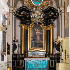 Zdjęcie nr 1: Przyścienna, jednoosiowa i jednokondygnacyjna struktura ołtarza uzyskała kształt nastawy architektonicznej ze zwieńczeniem. Drewniany stipes ołtarzowy przyjął formę leżącego prostopadłościanu podtrzymującego mensę, ustawionego na dwustopniowym podeście. Drewniane antependium ujęto profilowaną ramą z polem udekorowanym monogramem maryjnym w centrum, otoczonym rzeźbionym różańcem przy zewnętrznych krawędziach. Stipes przylega do  trzystrefowego, wysokiego cokołu wspierającego nastawę. Kolejne strefy zostały wydzielone za pomocą poziomych profili. Drugą i trzecią strefę cokołu ozdobiono obramionymi, prostokątnymi płycinami - w drugiej strefie w kształcie stojących prostokątów, a w trzeciej leżących. Kondygnację wsparto na zdwojonych pilastrach o korynckich głowicach, przed którymi ustawiono korynckie kolumny podtrzymujące imposty ze wspartym na nim przerwanym belkowaniem wyłamanym na ich osi. Na belkowaniu widoczne są dwa półkoliste przyczółki z klęczącymi na nich dwoma aniołkami. W kondygnacji pomiędzy pilastrami i kolumnami usytuowano pole obrazowe obramienione profilowaną ramą w kształcie stojącego prostokąta zwieńczonego nadwieszonym łukiem odcinkowym. Rama ujmuje obraz przedstawiający św. Józefa z Dzieciątkiem Jezus. Kondygnację flankują ustawione na cokole retabulum figury św. Dominika i św. Katarzyny ze Sieny. Na osi pola obrazowego w kondygnacji, zawieszono na belkowaniu fantazyjny kartusz z monogramem maryjnym na tle obłoków z uskrzydlonymi główkami anielskimi, powyżej którego w zwieńczeniu retabulum znalazła się promienista gloria z chrystogramem &quot;IHS&quot; otoczonym koliście obłokami. Litery monogramu utworzono z płaskorzeźbionych, złoconych róż w niebieskim polu. W centrum litery &quot;H&quot; na konsolce ukazano w pełnej postaci stojące Dzieciątko Jezusa z rozłożonymi rękami. Struktura ołtarza została pomalowana na czarno, natomiast kolumny, głowice pilastrów, profile architektoniczne oraz glorię i skrzydła aniołków wyzłocono, obłoki w glorii posrebrzono, a pole antependium i glorii pomalowano na niebiesko. Rzeźby świętych dominikańskich, aniołów i Dzieciątka Jezus uzyskały naturalistyczną polichromię.  