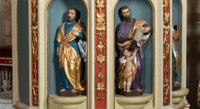 Zdjęcie nr 1: Kosz ambony wykonano na rzucie ośmioboku, wspartego na ośmiobocznym cokole. Bok kosza artykułują pilastry o kompozytowych głowicach i dekorowanych arabeską trzonach, wspartych na postumentach ozdobionych ornamentem geometrycznym. Pilastry podtrzymują profilowane belkowanie wyłamane na ich osi. Pomiędzy pilastrami umieszczono półokrągłe nisze zaopatrzone u spodu w półokrągłe konsole. W niszach ustawiono całopostaciowe, rzeźbione przedstawienia czterech Ewangelistów. Pod amboną podwieszono wolutowe spływy łączące cokół kolejnego pilastru ze znajdującą się na spodzie podwieszenia dekoracyjną szyszką. Na belkowaniu na osi usytuowano pulpit w formie rozwiniętego zwoju pisarskiego wspartego na powiększonym kapitelu kompozytowym, wzorowanym na kapitelu z pilastrów bocznych. Strukturę architektoniczną kosza polichromowanego w kolorze ciemnej kości słoniowej, wnętrze wnęk na niebiesko, a tło trzonów kapiteli i ich głowic na czerwono. Rzeźby czterech Ewangelistów uzyskały polichromię naturalistyczną. 