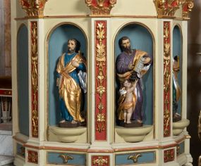 Zdjęcie nr 1: Kosz ambony wykonano na rzucie ośmioboku, wspartego na ośmiobocznym cokole. Bok kosza artykułują pilastry o kompozytowych głowicach i dekorowanych arabeską trzonach, wspartych na postumentach ozdobionych ornamentem geometrycznym. Pilastry podtrzymują profilowane belkowanie wyłamane na ich osi. Pomiędzy pilastrami umieszczono półokrągłe nisze zaopatrzone u spodu w półokrągłe konsole. W niszach ustawiono całopostaciowe, rzeźbione przedstawienia czterech Ewangelistów. Pod amboną podwieszono wolutowe spływy łączące cokół kolejnego pilastru ze znajdującą się na spodzie podwieszenia dekoracyjną szyszką. Na belkowaniu na osi usytuowano pulpit w formie rozwiniętego zwoju pisarskiego wspartego na powiększonym kapitelu kompozytowym, wzorowanym na kapitelu z pilastrów bocznych. Strukturę architektoniczną kosza polichromowanego w kolorze ciemnej kości słoniowej, wnętrze wnęk na niebiesko, a tło trzonów kapiteli i ich głowic na czerwono. Rzeźby czterech Ewangelistów uzyskały polichromię naturalistyczną. 