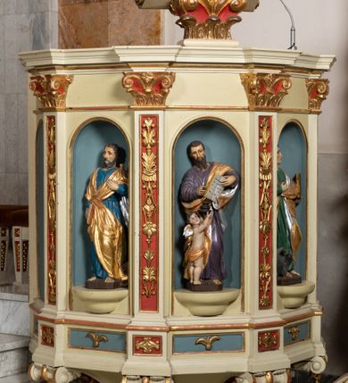 Zdjęcie nr 2: Kosz ambony wykonano na rzucie ośmioboku, wspartego na ośmiobocznym cokole. Bok kosza artykułują pilastry o kompozytowych głowicach i dekorowanych arabeską trzonach, wspartych na postumentach ozdobionych ornamentem geometrycznym. Pilastry podtrzymują profilowane belkowanie wyłamane na ich osi. Pomiędzy pilastrami umieszczono półokrągłe nisze zaopatrzone u spodu w półokrągłe konsole. W niszach ustawiono całopostaciowe, rzeźbione przedstawienia czterech Ewangelistów. Pod amboną podwieszono wolutowe spływy łączące cokół kolejnego pilastru ze znajdującą się na spodzie podwieszenia dekoracyjną szyszką. Na belkowaniu na osi usytuowano pulpit w formie rozwiniętego zwoju pisarskiego wspartego na powiększonym kapitelu kompozytowym, wzorowanym na kapitelu z pilastrów bocznych. Strukturę architektoniczną kosza polichromowanego w kolorze ciemnej kości słoniowej, wnętrze wnęk na niebiesko, a tło trzonów kapiteli i ich głowic na czerwono. Rzeźby czterech Ewangelistów uzyskały polichromię naturalistyczną. 