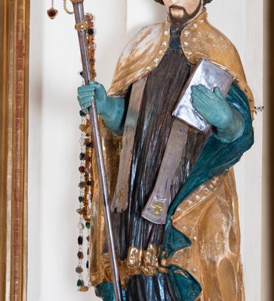 Zdjęcie nr 5: Przyścienny, jednokondygnacyjny ołtarz boczny uzyskał strukturę architektoniczną ze zwieńczeniem. Drewniany stipes ołtarzowy w formie prostopadłościanu, ustawiony na jednostopniowym podeście, podtrzymuję mensę. Jego lico zdobi aplikacja symbolizująca płonące Serce Jezusa w promienistym otoku. Retabulum ustawiono na wysokim dwupoziomowym cokole. Pierwszy poziom tworzy prostopadłościenna struktura dekorowana dwiema płycinami w formie stojącego prostokąta zwieńczona profilowanym gzymsem. Nad drugi poziomie znalazła się przerwana w osi środkowej wklęsło-wypułka strefa cokołowa z płycinami ozdobionymi czworobokami ze stylizowanego ornamentu roślinnego. Wspiera ona flankujące kondygnację dwa pilastry z głowicami wolutowymi o trzonach zdobionych zwisami roślinnymi na wstęgach oraz dwie kolumny z kapitelami kompozytowymi. Podpory podtrzymują belkowanie półkoliście wyłamane na osi pilastrów z rozbudowanym architrawem, powtarzającym układ górnej strefy cokołowej. Po bokach nastawy widoczne są dwa uszaki zredukowane do ażurowej wici roślinnej. Zwieńczenie uzyskało kształt leżącego prostokąta z wklęsłymi bokami przechodzącymi w spływy wolutowe. Wieńczy je gzyms koronujący w kształcie nadwieszonego łuku odcinkowego z podwieszonym ornamentem liściastym. Na gzymsie ustawiono na osi krzyż. W polu kondygnacji umieszczono pole obrazowe w kształcie stojącego prostokąta zamknięte profilowaną ramą z wyobrażeniem Najświętszego Serca Pana Jezusa. Ujmuje go figura św. Jana Kantego i św. Biskupa ustawione na półkoliście wyłamanych fragmentach cokołu. W zwieńczenia umieszczono w owalu obraz św. Tekli. Strukturę polichromowano w kolorze kości słoniowej oraz beżowej, natomiast kolumny, partie ornamentu, profile pozłocono. 