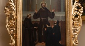 Zdjęcie nr 1: Czworoboczne pole obrazowe w kształcie stojącego prostokąta, ujęte w dekoracyjną ramę ze zwieńczeniem oraz ażurową wicią akantowo-kwiatową po bokach, ustawiono na postumencie w kształcie leżącego prostopadłościanu dekorowanego profilami o wklęsłych bokach z wywiniętym ornamentem roślinnym. Całość przytwierdzonym do prostopadłościennego cokołu, profilowanego i fazowanego, przeprutego po bokach otworami na drążki do noszenia, wspartego na czterech rzeźbionych lwich łapach. Zwieńczenie uzyskało kształt półkolistego pola z krzyżem równoramiennym w otoku w środku, ujętego dekoracyjną ramą otoczoną na zewnątrz ażurowym ornamentem, zakończonego na szczycie krzyżem. Na awersie w polu obrazowym umieszczono obraz z adoracja św. Franciszka z Asyżu. Święty został ukazany frontalnie stojąc w centrum kompozycji na stopniu przed ołtarzem. Obie rozłożone ręce z widocznymi stygmatami ma uniesione w górze. Prawą zdaje się błogosławić klęczącą przed nim parę. Franciszek ma pociągłą twarz o jasnej karnacji z półprzymkniętymi oczami o spojrzeniu skierowanym na klęczących z wydatnym nosem i ustami. Jego głowę otaczają krótkie włosy z wyciętą tonsurą oraz brązową broda. Ubrany jest w brązowy habit franciszkańskie przewiązany w pasie sznurem. Przed nim z prawej strony kompozycji klęczy kobieta z mężczyzną ujęci od tyłu w trzech czwartych w prawo. Oboje mają modlitewnie złożone dłonie. Mężczyzna ma ciemne włosy i zarost, ubrany jest w surdut. Kobieta ma krótko upięte włosy oraz czarną suknię z białym kołnierzykiem. Z lewej strony kompozycji stoi brodaty franciszkanin z tonsurą ujęty w profilu w prawo. W lewej ręce trzyma złożony habit, a w prawej sznur. Za Franciszkiem znajduje się prostopadłościenny ołtarz nakryty białym obrusem z ustawionym na nim krucyfiksem i czterema płonącymi świecami w wysokich lichtarzach. Tło dla ołtarza tworzy szarobeżowa wnęka flankowana dwiema lizenami. Na rewersie wyobrażono Niepokalane Poczęcie Najświętszej Marii Panny. W centrum kompozycji znalazła się wyobrażona w całej postaci w mocnym kontrapoście Madonna stojąca na półksiężycu na obłokach. Maria obie dłonie ma skrzyżowane na piersiach. Jej głowa została ujęta w trzech czwartych w prawo. Jest to młoda dziewczyna o pociągłej twarzy, jasnej karnacji wydatnym nosie i pełnych ustach. Jej spojrzenie uniesionych oczu skierowane jest w górę. Głowę otaczają długie, brązowe włosy spływające na plecy oraz świetlista poświata z dwunastoma gwiazdkami. Niepokalana ubrana jest w białą suknię przewiązaną w talli oraz niebieski płaszcz przerzucony przez lewe ramię, którego poły opadają na obłoki. Ponad głową Marii dwa putta unoszą zamkniętą, złotą koronę. Po jej bokach na rozjaśnionym tle na obłokach wyobrażono dwie pary uskrzydlonych aniołków. Pozostałych pięć aniołków igra pośród obłoków poniżej półksiężyca, na którym wspiera się Maria. 