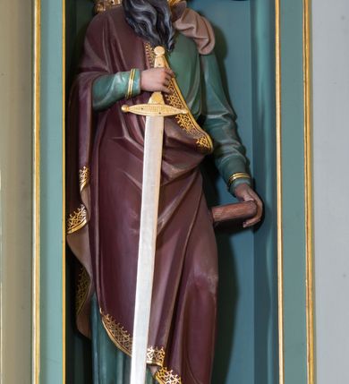 Zdjęcie nr 3: Nastawa ołtarza głównego przyjęła formę przyściennej, trójosiowej, jednokondygnacyjnej struktury architektonicznej ze wieńczeniem. Drewniany stipes ołtarzowy uzyskał kształt leżącego prostopadłościanu podtrzymującego mensę z portatylem, ustawionego na jednostopniowym podeście. Front stipesu udekorowano trzema płycinami obwiedzionymi profilowanymi listwami z rzeźbionymi ornamentami w polach. Na mensie ustawiono drewniane tabernakulum na rzucie trapezu. W dolnej części artykułują je czworoboczne płyciny z ornamentem geometrycznym, rozdzielone spływami wolutowymi podtrzymującymi profilowany gzyms, a w górnej części rozbudowany tron wystawienia. Prostopadłościenne, pancerne tabernakulum usytuowano na osi zdobiąc jego czworoboczne drzwiczki płyciną z trybowanym przedstawieniem kielicha w otoczeniu winnej latorośli i kłosów zbóż. Tron wystawienia przyjął formę trójarkadowej kapliczki zwieńczonej gzymsem koronującym i spłaszczonym dachem pokrytym złoconą rybią łuską. Arkady wsparto na korynckich, kanelowanych kolumienkach. W przyłuczach arkady środkowej, wypełnionej niszą na monstrancję, ukazano uskrzydlone dwie główki anielskie, a w przyłuczach arkad skrajnych motywy ornamentalne. Pod arkadami w osiach skrajnych umieszczono w niszach klęczących na jedno kolana na postumentach adorujących aniołów. Wsparty na arkadach gzyms koronujący ozdobiono profilowaniem i rytmicznie powtarzającymi się konsolkami. Za stipesem ustawiono strukturę ołtarzowa wspartą na wysokim cokole, artykułowaną czterema wysuniętym do przodu dwustopniowymi postumentami dekorowanymi profilowanym gzymsowaniem oraz prostokątnymi płycinami ujętymi w profilowane obramienia. W górnej strefie w płycinach od frontu wyobrażono uskrzydlone głowy symboli czterech Ewangelistów. Idę od lewej jest to głowa woła, anioła, orła i lwa. Natomiast w dolne strefie w płycinach znalazły się od lewej: skrzyżowane bicze z trzciną, na tle których wyobrażono chustę Weroniki, świecznik siedmioramienny z miedzianym wężem na palu na tle pektorału żydowskiego arcykapłana, tablice Dekalogu na tle skrzyżowanych trąb oraz krzyż skrzyżowany z kolumną biczowania wraz z lancą i gąbką na kiju. Pomiędzy postumentami w osiach skrajnych partii cokołowej usytuowano dwoje drzwi prowadzących do zakrystii, zdobionych czworobocznymi płycinami. Na postumentach ustawiono cztery kanelowane kolumny o kapitelach kompozytowych z impostami podtrzymujących belkowanie wyłamane na ich osi. Pomiędzy kolumnami artykułującymi kondygnację w osi środkowej umieszczono pole obrazowe, a w osiach skrajnych półkoliste nisze z ustawionymi w nich na postumentach figurami ŚŚ. Apostołów Piotra i Pawła. Zarówno nad polem obrazowym, jak i nad niszami oraz pod nimi widoczny jest ornament roślinny. Pole obrazowe na osi retabulum przyjęło kształt stojącego prostokąta z nadwieszonym półkolistym łukiem odcinkowym. Ujmuje je profilowana rama. W polu umieszczono obraz Wniebowzięcia Najświętszej Marii Panny, a na dwóch zasuwach przedstawienie św. Urbana oraz św. Barbary. Na belkowaniu w osiach skrajnych nad kolumnami zewnętrznymi usytuowano dwa przerwane przyczółki z leżącymi na nich parą aniołów trzymających krzyż i kotwicę. Natomiast na osi kolumn wewnętrznych na postumentach siedzą dwa złocone putta. Zwieńczenie ołtarza przyjęło kształt leżącego prostokąta flankowanego przez pilaster i kolumienkę podtrzymujących odcinki wyłamanego belkowania, na którym wsparto półkolisty, profilowany łuk odcinkowy wieńczący całość. Ponad tymi podporami umieszczono złocone, siedzące putta, a na osi łuku wieńczącego w promieniach z obłoczkami gołębicę Ducha Świętego. W polu zwieńczenia usytuowano półkolistą niszę ze stojącą figurą Boga Ojca. Ujmuje ją półkoliste obramienie zdobione stylizowaną ornamentyką roślinno-geometryczną. Strukturę architektoniczną retabulum polichromowano w tonacji jasnopastelowej zieleni, ornamenty, profile architektoniczne zostały wyzłocone, natomiast figury apostołów, Boga Ojca oraz aniołów przy tabernakulum i w zwieńczeniu w osiach skrajnych zostały naturalistycznie polichromowane. 