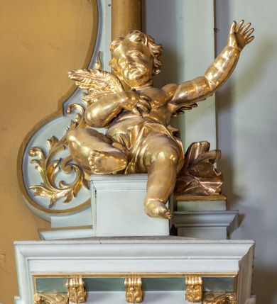 Zdjęcie nr 16: Nastawa ołtarza głównego przyjęła formę przyściennej, trójosiowej, jednokondygnacyjnej struktury architektonicznej ze wieńczeniem. Drewniany stipes ołtarzowy uzyskał kształt leżącego prostopadłościanu podtrzymującego mensę z portatylem, ustawionego na jednostopniowym podeście. Front stipesu udekorowano trzema płycinami obwiedzionymi profilowanymi listwami z rzeźbionymi ornamentami w polach. Na mensie ustawiono drewniane tabernakulum na rzucie trapezu. W dolnej części artykułują je czworoboczne płyciny z ornamentem geometrycznym, rozdzielone spływami wolutowymi podtrzymującymi profilowany gzyms, a w górnej części rozbudowany tron wystawienia. Prostopadłościenne, pancerne tabernakulum usytuowano na osi zdobiąc jego czworoboczne drzwiczki płyciną z trybowanym przedstawieniem kielicha w otoczeniu winnej latorośli i kłosów zbóż. Tron wystawienia przyjął formę trójarkadowej kapliczki zwieńczonej gzymsem koronującym i spłaszczonym dachem pokrytym złoconą rybią łuską. Arkady wsparto na korynckich, kanelowanych kolumienkach. W przyłuczach arkady środkowej, wypełnionej niszą na monstrancję, ukazano uskrzydlone dwie główki anielskie, a w przyłuczach arkad skrajnych motywy ornamentalne. Pod arkadami w osiach skrajnych umieszczono w niszach klęczących na jedno kolana na postumentach adorujących aniołów. Wsparty na arkadach gzyms koronujący ozdobiono profilowaniem i rytmicznie powtarzającymi się konsolkami. Za stipesem ustawiono strukturę ołtarzowa wspartą na wysokim cokole, artykułowaną czterema wysuniętym do przodu dwustopniowymi postumentami dekorowanymi profilowanym gzymsowaniem oraz prostokątnymi płycinami ujętymi w profilowane obramienia. W górnej strefie w płycinach od frontu wyobrażono uskrzydlone głowy symboli czterech Ewangelistów. Idę od lewej jest to głowa woła, anioła, orła i lwa. Natomiast w dolne strefie w płycinach znalazły się od lewej: skrzyżowane bicze z trzciną, na tle których wyobrażono chustę Weroniki, świecznik siedmioramienny z miedzianym wężem na palu na tle pektorału żydowskiego arcykapłana, tablice Dekalogu na tle skrzyżowanych trąb oraz krzyż skrzyżowany z kolumną biczowania wraz z lancą i gąbką na kiju. Pomiędzy postumentami w osiach skrajnych partii cokołowej usytuowano dwoje drzwi prowadzących do zakrystii, zdobionych czworobocznymi płycinami. Na postumentach ustawiono cztery kanelowane kolumny o kapitelach kompozytowych z impostami podtrzymujących belkowanie wyłamane na ich osi. Pomiędzy kolumnami artykułującymi kondygnację w osi środkowej umieszczono pole obrazowe, a w osiach skrajnych półkoliste nisze z ustawionymi w nich na postumentach figurami ŚŚ. Apostołów Piotra i Pawła. Zarówno nad polem obrazowym, jak i nad niszami oraz pod nimi widoczny jest ornament roślinny. Pole obrazowe na osi retabulum przyjęło kształt stojącego prostokąta z nadwieszonym półkolistym łukiem odcinkowym. Ujmuje je profilowana rama. W polu umieszczono obraz Wniebowzięcia Najświętszej Marii Panny, a na dwóch zasuwach przedstawienie św. Urbana oraz św. Barbary. Na belkowaniu w osiach skrajnych nad kolumnami zewnętrznymi usytuowano dwa przerwane przyczółki z leżącymi na nich parą aniołów trzymających krzyż i kotwicę. Natomiast na osi kolumn wewnętrznych na postumentach siedzą dwa złocone putta. Zwieńczenie ołtarza przyjęło kształt leżącego prostokąta flankowanego przez pilaster i kolumienkę podtrzymujących odcinki wyłamanego belkowania, na którym wsparto półkolisty, profilowany łuk odcinkowy wieńczący całość. Ponad tymi podporami umieszczono złocone, siedzące putta, a na osi łuku wieńczącego w promieniach z obłoczkami gołębicę Ducha Świętego. W polu zwieńczenia usytuowano półkolistą niszę ze stojącą figurą Boga Ojca. Ujmuje ją półkoliste obramienie zdobione stylizowaną ornamentyką roślinno-geometryczną. Strukturę architektoniczną retabulum polichromowano w tonacji jasnopastelowej zieleni, ornamenty, profile architektoniczne zostały wyzłocone, natomiast figury apostołów, Boga Ojca oraz aniołów przy tabernakulum i w zwieńczeniu w osiach skrajnych zostały naturalistycznie polichromowane. 