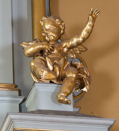 Zdjęcie nr 18: Nastawa ołtarza głównego przyjęła formę przyściennej, trójosiowej, jednokondygnacyjnej struktury architektonicznej ze wieńczeniem. Drewniany stipes ołtarzowy uzyskał kształt leżącego prostopadłościanu podtrzymującego mensę z portatylem, ustawionego na jednostopniowym podeście. Front stipesu udekorowano trzema płycinami obwiedzionymi profilowanymi listwami z rzeźbionymi ornamentami w polach. Na mensie ustawiono drewniane tabernakulum na rzucie trapezu. W dolnej części artykułują je czworoboczne płyciny z ornamentem geometrycznym, rozdzielone spływami wolutowymi podtrzymującymi profilowany gzyms, a w górnej części rozbudowany tron wystawienia. Prostopadłościenne, pancerne tabernakulum usytuowano na osi zdobiąc jego czworoboczne drzwiczki płyciną z trybowanym przedstawieniem kielicha w otoczeniu winnej latorośli i kłosów zbóż. Tron wystawienia przyjął formę trójarkadowej kapliczki zwieńczonej gzymsem koronującym i spłaszczonym dachem pokrytym złoconą rybią łuską. Arkady wsparto na korynckich, kanelowanych kolumienkach. W przyłuczach arkady środkowej, wypełnionej niszą na monstrancję, ukazano uskrzydlone dwie główki anielskie, a w przyłuczach arkad skrajnych motywy ornamentalne. Pod arkadami w osiach skrajnych umieszczono w niszach klęczących na jedno kolana na postumentach adorujących aniołów. Wsparty na arkadach gzyms koronujący ozdobiono profilowaniem i rytmicznie powtarzającymi się konsolkami. Za stipesem ustawiono strukturę ołtarzowa wspartą na wysokim cokole, artykułowaną czterema wysuniętym do przodu dwustopniowymi postumentami dekorowanymi profilowanym gzymsowaniem oraz prostokątnymi płycinami ujętymi w profilowane obramienia. W górnej strefie w płycinach od frontu wyobrażono uskrzydlone głowy symboli czterech Ewangelistów. Idę od lewej jest to głowa woła, anioła, orła i lwa. Natomiast w dolne strefie w płycinach znalazły się od lewej: skrzyżowane bicze z trzciną, na tle których wyobrażono chustę Weroniki, świecznik siedmioramienny z miedzianym wężem na palu na tle pektorału żydowskiego arcykapłana, tablice Dekalogu na tle skrzyżowanych trąb oraz krzyż skrzyżowany z kolumną biczowania wraz z lancą i gąbką na kiju. Pomiędzy postumentami w osiach skrajnych partii cokołowej usytuowano dwoje drzwi prowadzących do zakrystii, zdobionych czworobocznymi płycinami. Na postumentach ustawiono cztery kanelowane kolumny o kapitelach kompozytowych z impostami podtrzymujących belkowanie wyłamane na ich osi. Pomiędzy kolumnami artykułującymi kondygnację w osi środkowej umieszczono pole obrazowe, a w osiach skrajnych półkoliste nisze z ustawionymi w nich na postumentach figurami ŚŚ. Apostołów Piotra i Pawła. Zarówno nad polem obrazowym, jak i nad niszami oraz pod nimi widoczny jest ornament roślinny. Pole obrazowe na osi retabulum przyjęło kształt stojącego prostokąta z nadwieszonym półkolistym łukiem odcinkowym. Ujmuje je profilowana rama. W polu umieszczono obraz Wniebowzięcia Najświętszej Marii Panny, a na dwóch zasuwach przedstawienie św. Urbana oraz św. Barbary. Na belkowaniu w osiach skrajnych nad kolumnami zewnętrznymi usytuowano dwa przerwane przyczółki z leżącymi na nich parą aniołów trzymających krzyż i kotwicę. Natomiast na osi kolumn wewnętrznych na postumentach siedzą dwa złocone putta. Zwieńczenie ołtarza przyjęło kształt leżącego prostokąta flankowanego przez pilaster i kolumienkę podtrzymujących odcinki wyłamanego belkowania, na którym wsparto półkolisty, profilowany łuk odcinkowy wieńczący całość. Ponad tymi podporami umieszczono złocone, siedzące putta, a na osi łuku wieńczącego w promieniach z obłoczkami gołębicę Ducha Świętego. W polu zwieńczenia usytuowano półkolistą niszę ze stojącą figurą Boga Ojca. Ujmuje ją półkoliste obramienie zdobione stylizowaną ornamentyką roślinno-geometryczną. Strukturę architektoniczną retabulum polichromowano w tonacji jasnopastelowej zieleni, ornamenty, profile architektoniczne zostały wyzłocone, natomiast figury apostołów, Boga Ojca oraz aniołów przy tabernakulum i w zwieńczeniu w osiach skrajnych zostały naturalistycznie polichromowane. 