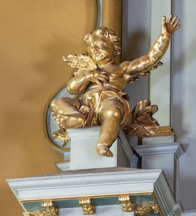 Zdjęcie nr 17: Nastawa ołtarza głównego przyjęła formę przyściennej, trójosiowej, jednokondygnacyjnej struktury architektonicznej ze wieńczeniem. Drewniany stipes ołtarzowy uzyskał kształt leżącego prostopadłościanu podtrzymującego mensę z portatylem, ustawionego na jednostopniowym podeście. Front stipesu udekorowano trzema płycinami obwiedzionymi profilowanymi listwami z rzeźbionymi ornamentami w polach. Na mensie ustawiono drewniane tabernakulum na rzucie trapezu. W dolnej części artykułują je czworoboczne płyciny z ornamentem geometrycznym, rozdzielone spływami wolutowymi podtrzymującymi profilowany gzyms, a w górnej części rozbudowany tron wystawienia. Prostopadłościenne, pancerne tabernakulum usytuowano na osi zdobiąc jego czworoboczne drzwiczki płyciną z trybowanym przedstawieniem kielicha w otoczeniu winnej latorośli i kłosów zbóż. Tron wystawienia przyjął formę trójarkadowej kapliczki zwieńczonej gzymsem koronującym i spłaszczonym dachem pokrytym złoconą rybią łuską. Arkady wsparto na korynckich, kanelowanych kolumienkach. W przyłuczach arkady środkowej, wypełnionej niszą na monstrancję, ukazano uskrzydlone dwie główki anielskie, a w przyłuczach arkad skrajnych motywy ornamentalne. Pod arkadami w osiach skrajnych umieszczono w niszach klęczących na jedno kolana na postumentach adorujących aniołów. Wsparty na arkadach gzyms koronujący ozdobiono profilowaniem i rytmicznie powtarzającymi się konsolkami. Za stipesem ustawiono strukturę ołtarzowa wspartą na wysokim cokole, artykułowaną czterema wysuniętym do przodu dwustopniowymi postumentami dekorowanymi profilowanym gzymsowaniem oraz prostokątnymi płycinami ujętymi w profilowane obramienia. W górnej strefie w płycinach od frontu wyobrażono uskrzydlone głowy symboli czterech Ewangelistów. Idę od lewej jest to głowa woła, anioła, orła i lwa. Natomiast w dolne strefie w płycinach znalazły się od lewej: skrzyżowane bicze z trzciną, na tle których wyobrażono chustę Weroniki, świecznik siedmioramienny z miedzianym wężem na palu na tle pektorału żydowskiego arcykapłana, tablice Dekalogu na tle skrzyżowanych trąb oraz krzyż skrzyżowany z kolumną biczowania wraz z lancą i gąbką na kiju. Pomiędzy postumentami w osiach skrajnych partii cokołowej usytuowano dwoje drzwi prowadzących do zakrystii, zdobionych czworobocznymi płycinami. Na postumentach ustawiono cztery kanelowane kolumny o kapitelach kompozytowych z impostami podtrzymujących belkowanie wyłamane na ich osi. Pomiędzy kolumnami artykułującymi kondygnację w osi środkowej umieszczono pole obrazowe, a w osiach skrajnych półkoliste nisze z ustawionymi w nich na postumentach figurami ŚŚ. Apostołów Piotra i Pawła. Zarówno nad polem obrazowym, jak i nad niszami oraz pod nimi widoczny jest ornament roślinny. Pole obrazowe na osi retabulum przyjęło kształt stojącego prostokąta z nadwieszonym półkolistym łukiem odcinkowym. Ujmuje je profilowana rama. W polu umieszczono obraz Wniebowzięcia Najświętszej Marii Panny, a na dwóch zasuwach przedstawienie św. Urbana oraz św. Barbary. Na belkowaniu w osiach skrajnych nad kolumnami zewnętrznymi usytuowano dwa przerwane przyczółki z leżącymi na nich parą aniołów trzymających krzyż i kotwicę. Natomiast na osi kolumn wewnętrznych na postumentach siedzą dwa złocone putta. Zwieńczenie ołtarza przyjęło kształt leżącego prostokąta flankowanego przez pilaster i kolumienkę podtrzymujących odcinki wyłamanego belkowania, na którym wsparto półkolisty, profilowany łuk odcinkowy wieńczący całość. Ponad tymi podporami umieszczono złocone, siedzące putta, a na osi łuku wieńczącego w promieniach z obłoczkami gołębicę Ducha Świętego. W polu zwieńczenia usytuowano półkolistą niszę ze stojącą figurą Boga Ojca. Ujmuje ją półkoliste obramienie zdobione stylizowaną ornamentyką roślinno-geometryczną. Strukturę architektoniczną retabulum polichromowano w tonacji jasnopastelowej zieleni, ornamenty, profile architektoniczne zostały wyzłocone, natomiast figury apostołów, Boga Ojca oraz aniołów przy tabernakulum i w zwieńczeniu w osiach skrajnych zostały naturalistycznie polichromowane. 