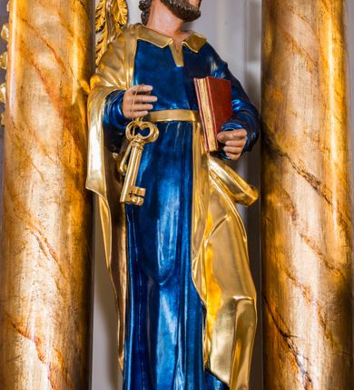 Zdjęcie nr 2: Drążona z tyłu, całopostaciowa figura przedstawia św. Piotra stojącego na niewysokiej podstawie i zwróconego na wprost. Skierowaną w trzech czwartych w lewo głowę charakteryzuje owalna twarz o wyrazistych, sumarycznie opracowanych rysach z długim spiczastym nosem, wystającymi kośćmi policzkowymi oraz krótkim zarostem. Włosy są krótkie z parą zakoli po bokach. Święty ubrany jest w ciemnoniebieską suknię ze złoconymi paskiem i kołnierzem oraz złocony płaszcz narzucony na prawe ramię i podwinięty pod pasek. Spod sukni widoczne bose stopy. W prawej ręce trzyma dwa złocone klucze, lewą podtrzymuje zamkniętą księgę w czerwonej oprawie.     